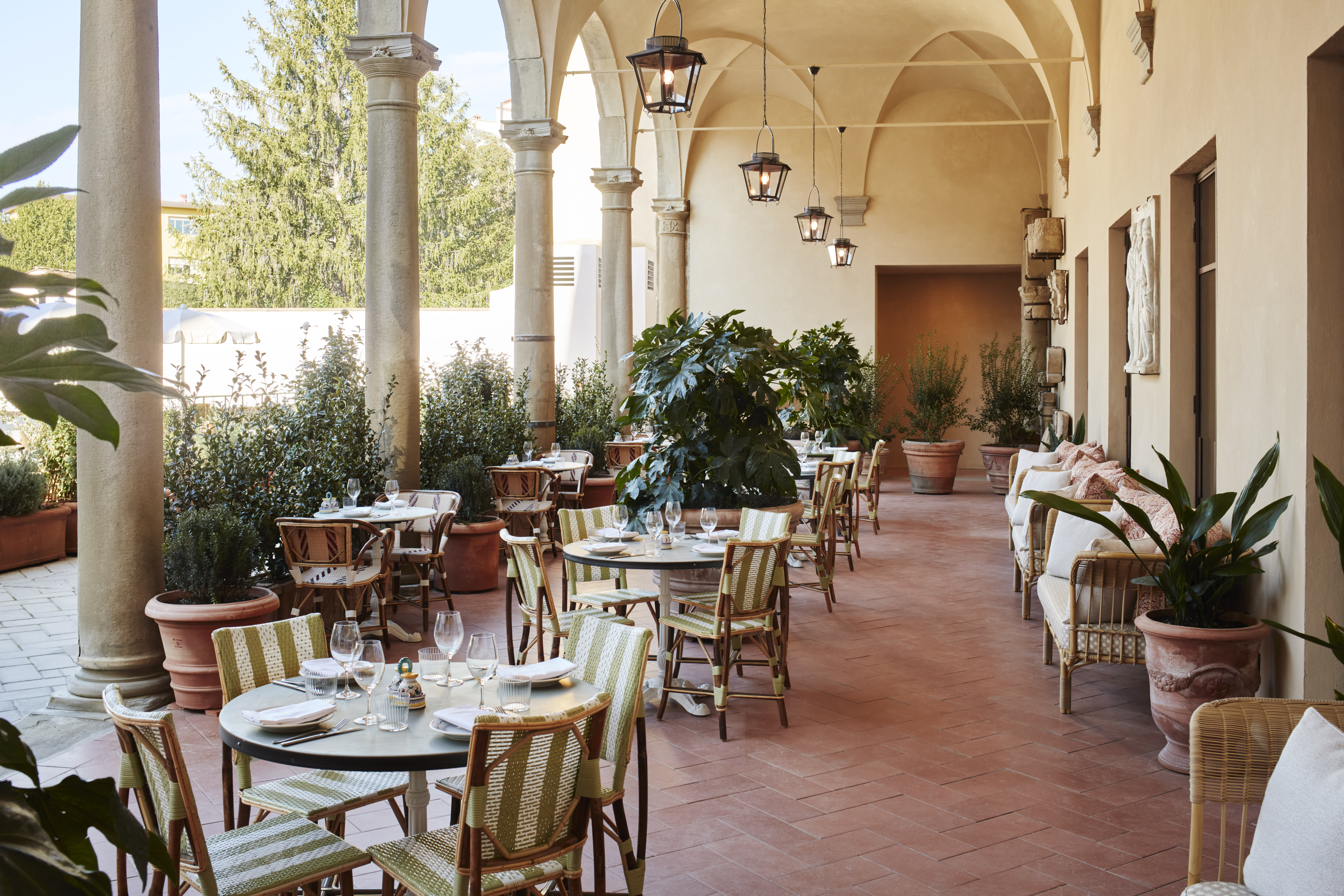 Outdoor terrace dining area with green-and-white striped chairs, round tables, potted plants, and vaulted ceiling arches.