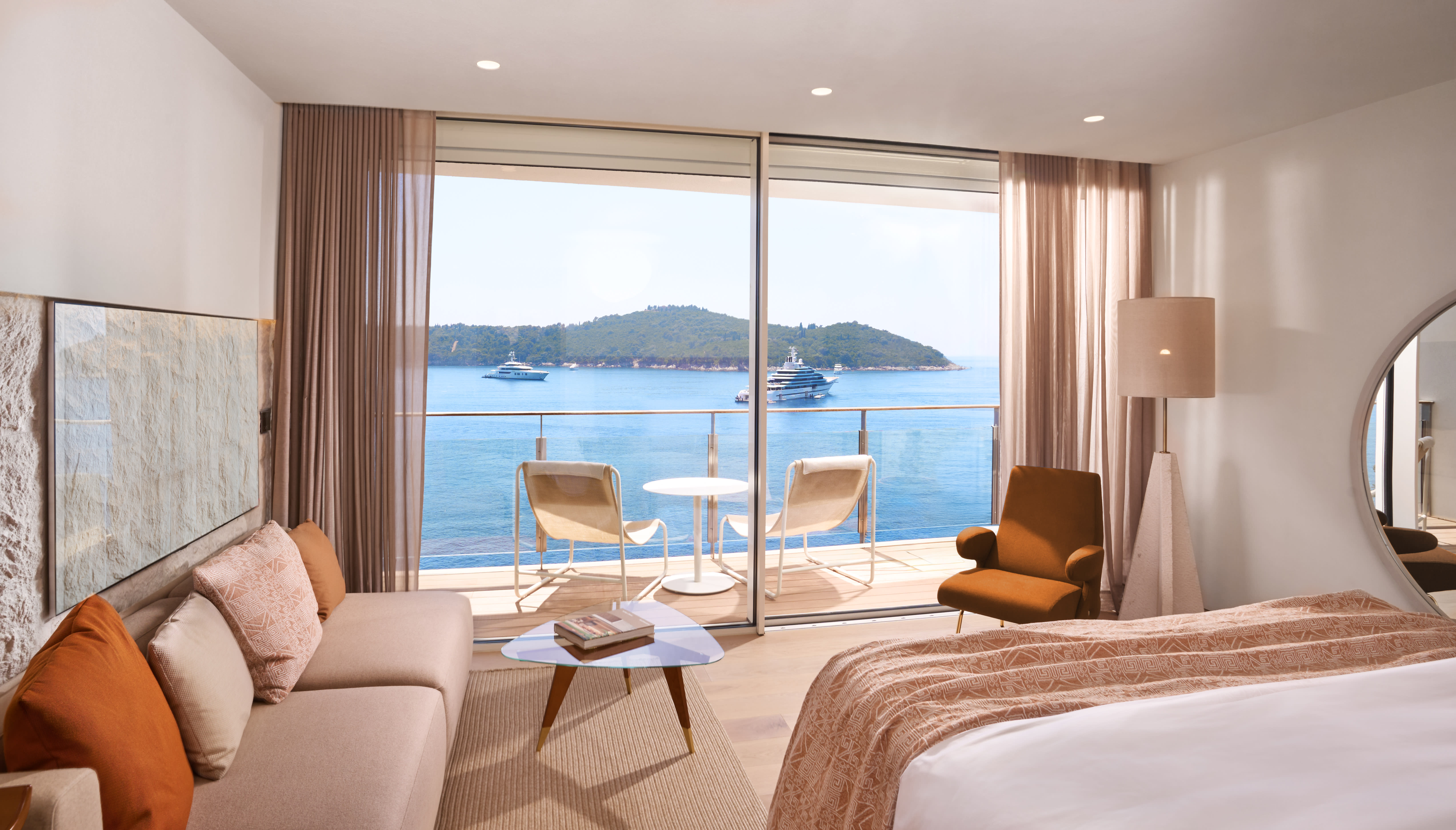 Bright modern hotel room with a seating area and balcony overlooking the blue Adriatic Sea and nearby islands.