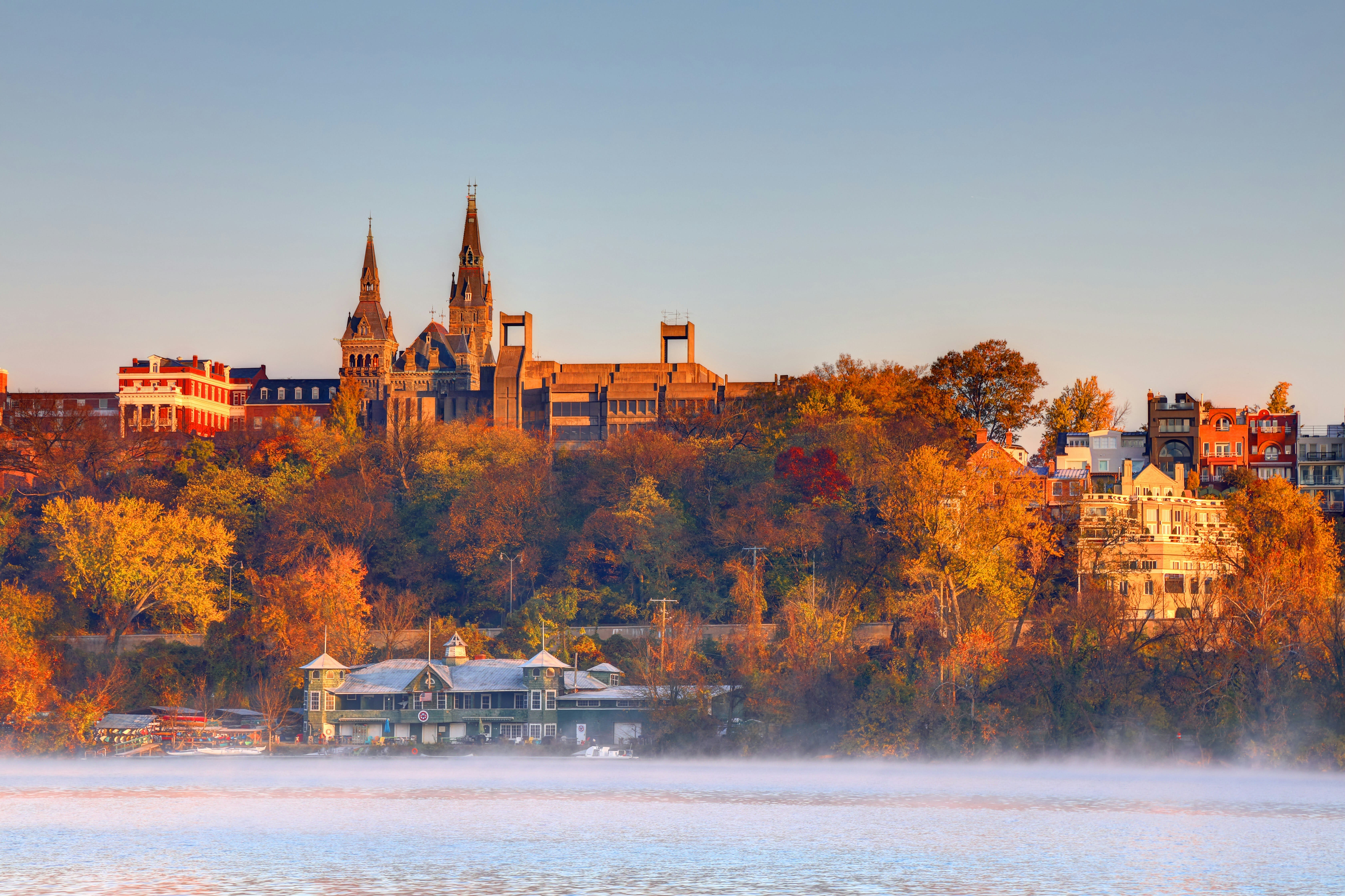 stone towers and buildings on a hill with fall foliage next to a fog covered river at dawn