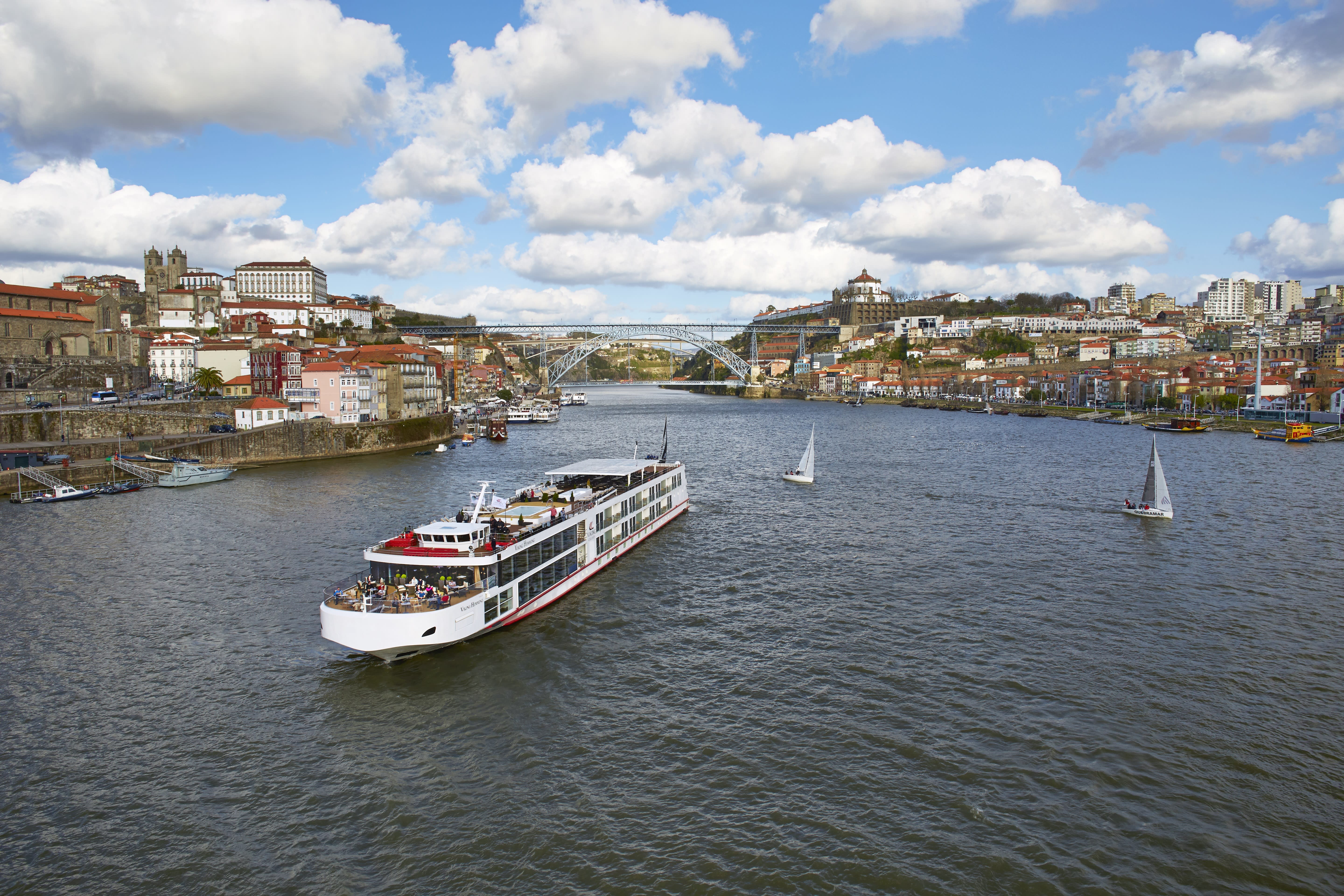small ship in a river surrounded by coastal towns in the background and a blue sky with clouds