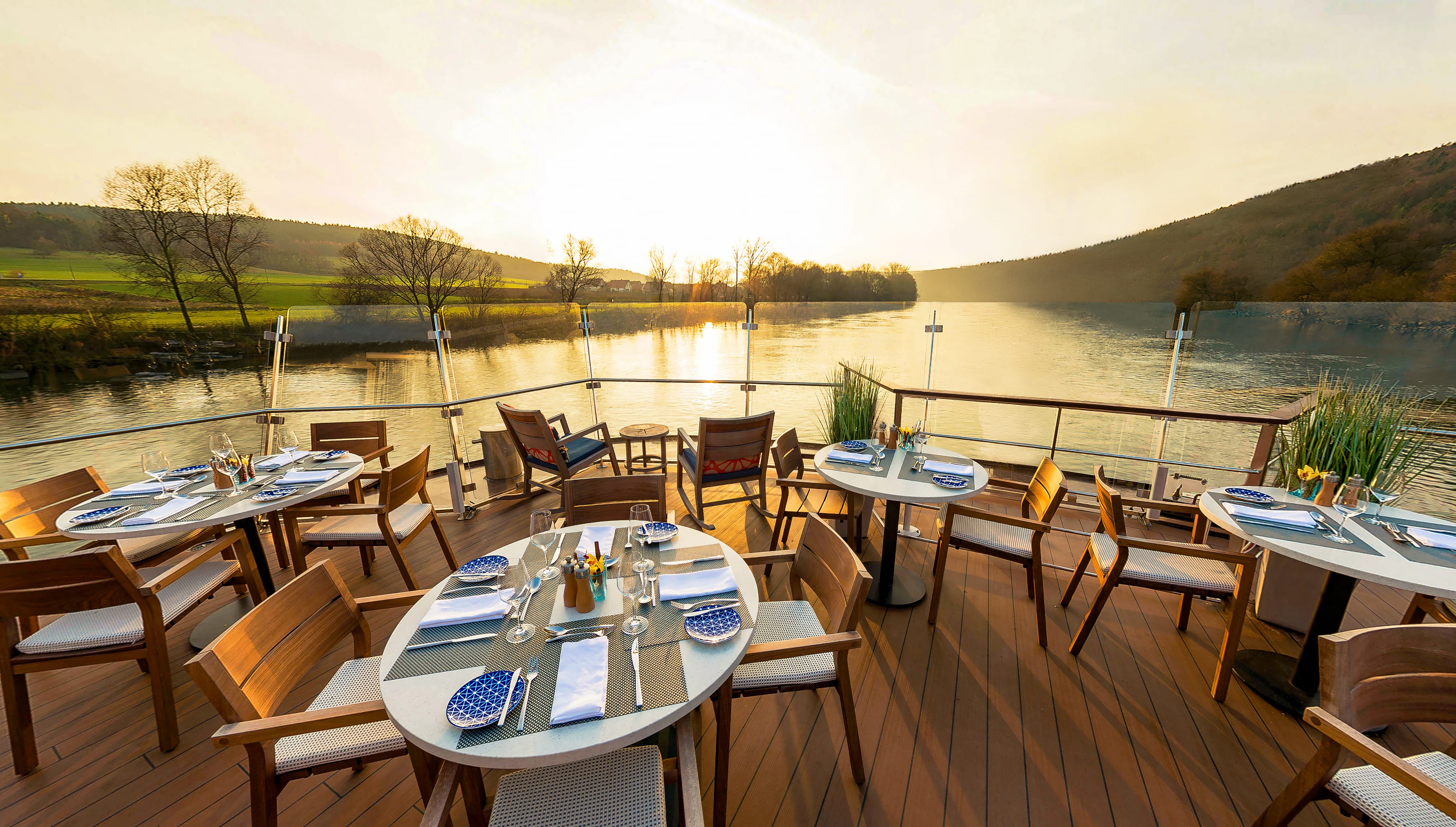 deck of a ship with tables and chairs set for a meal with river views