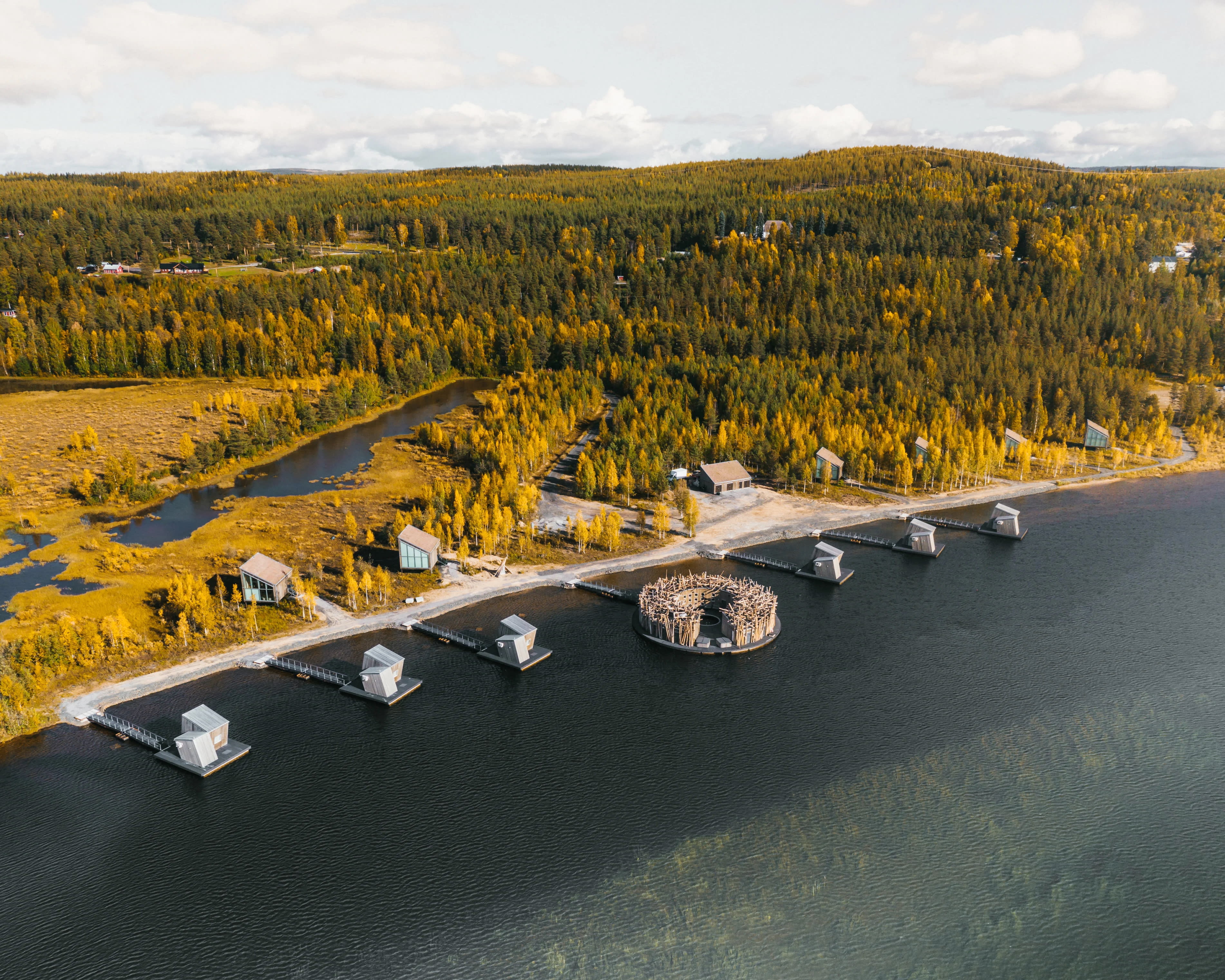 cabins floating on a river and on the riverbank with fall foliage forest behind during day