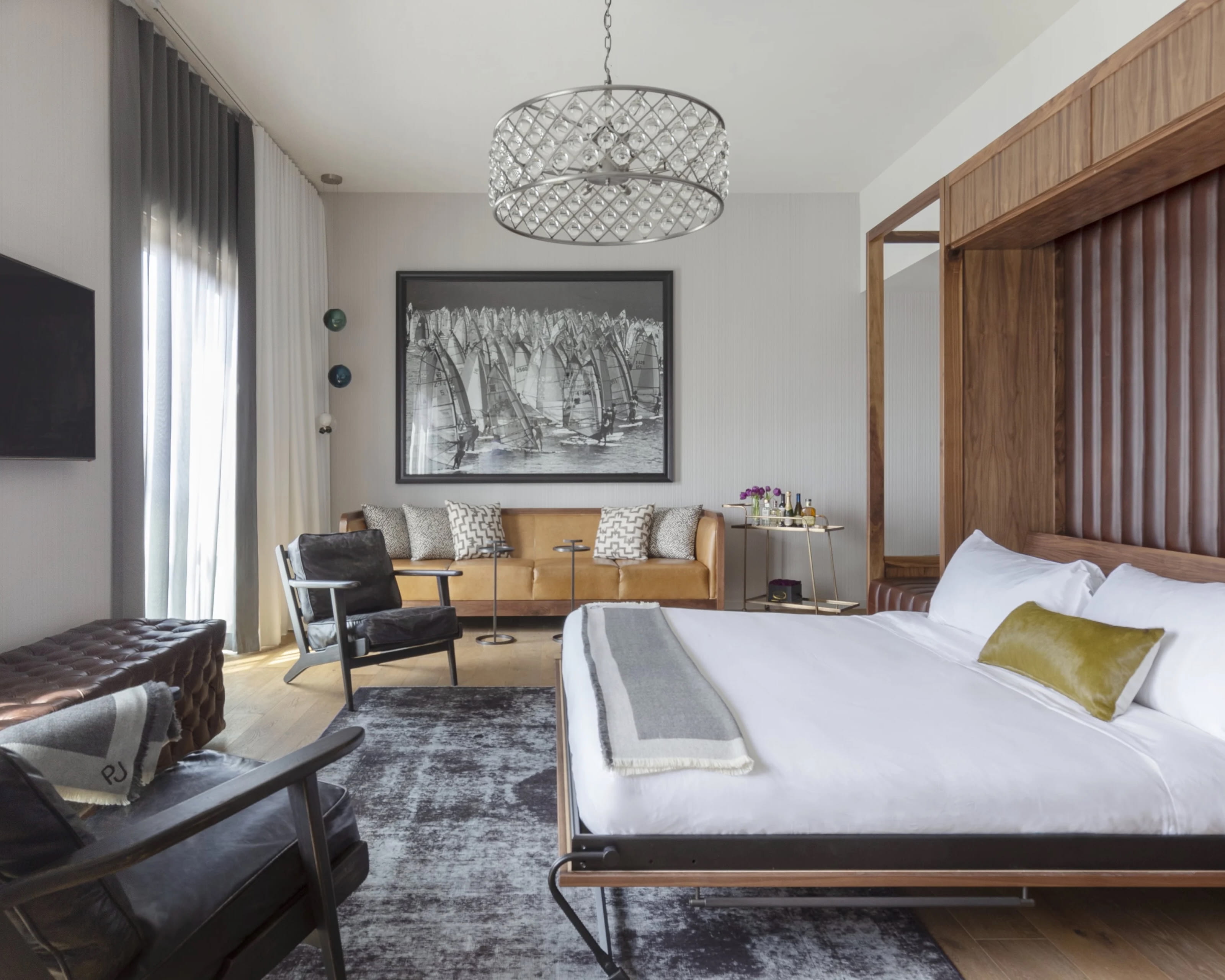 a modern hotel suite with tan wood, dark grey leather, and white bed linens