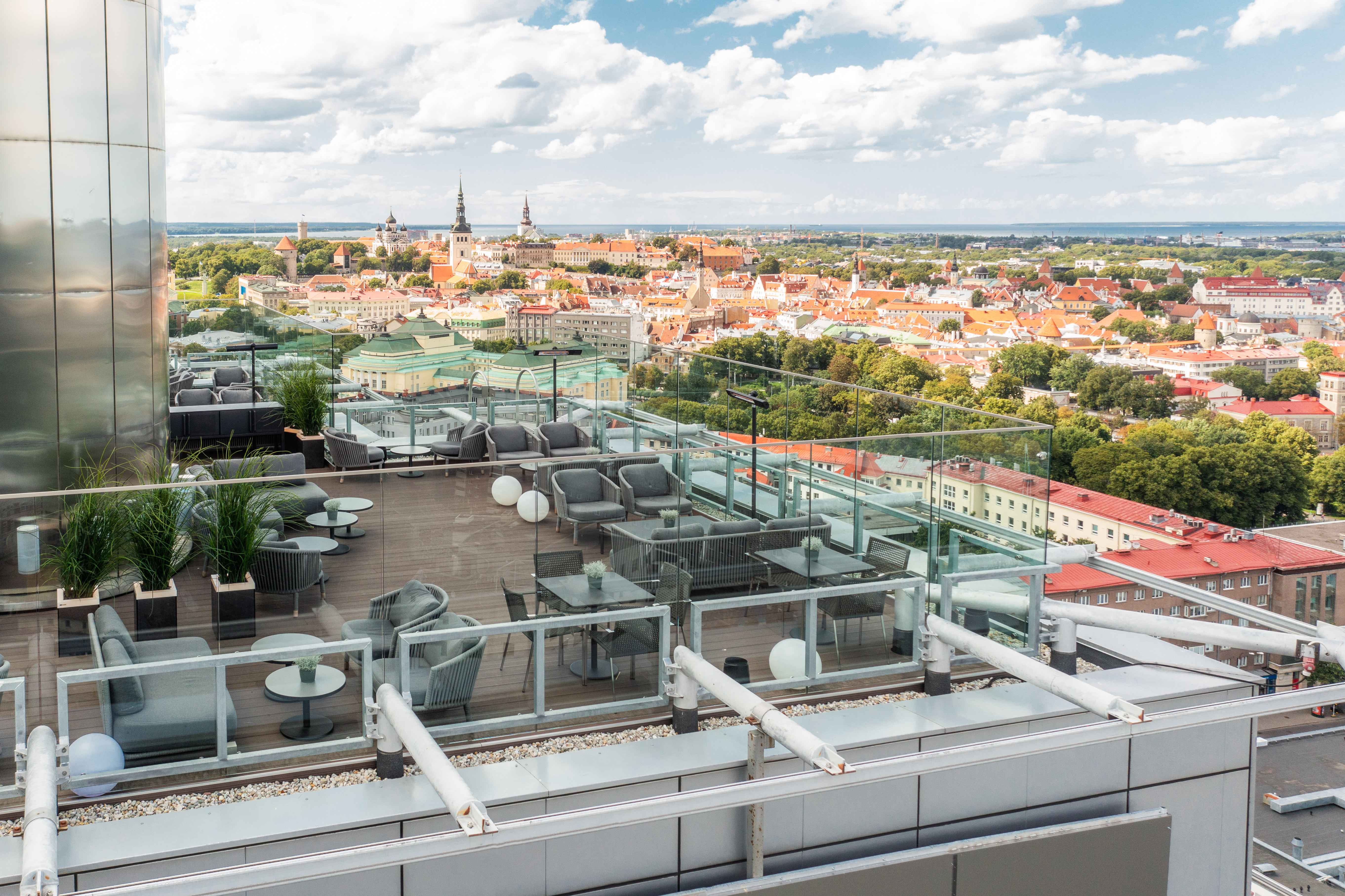 An aerial view of a rooftop bar with grey lounge seating and wooden flooring overlooking Tallinn, Estonia