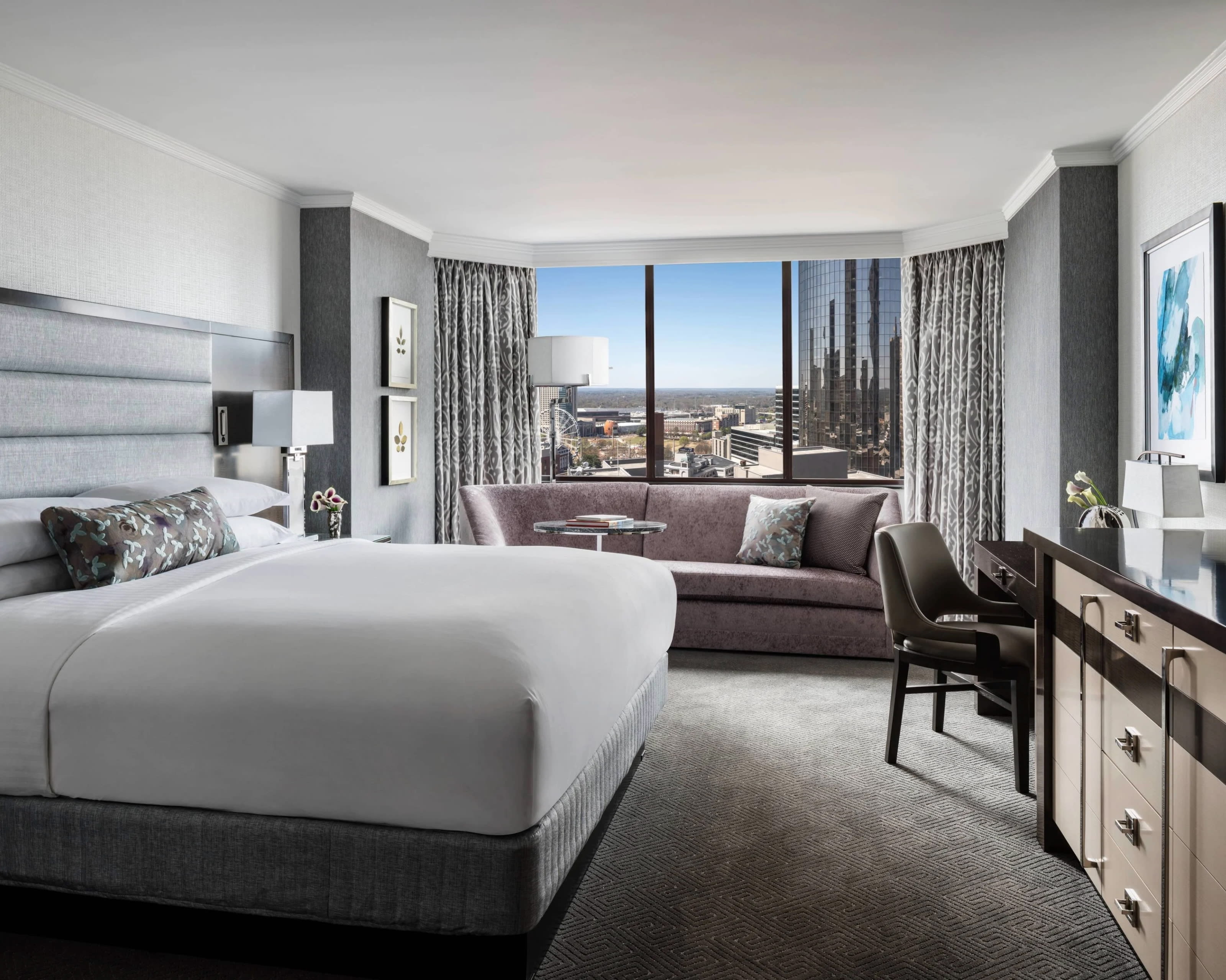 A white and grey hotel room with light purple sofa under the window and grey and white walls