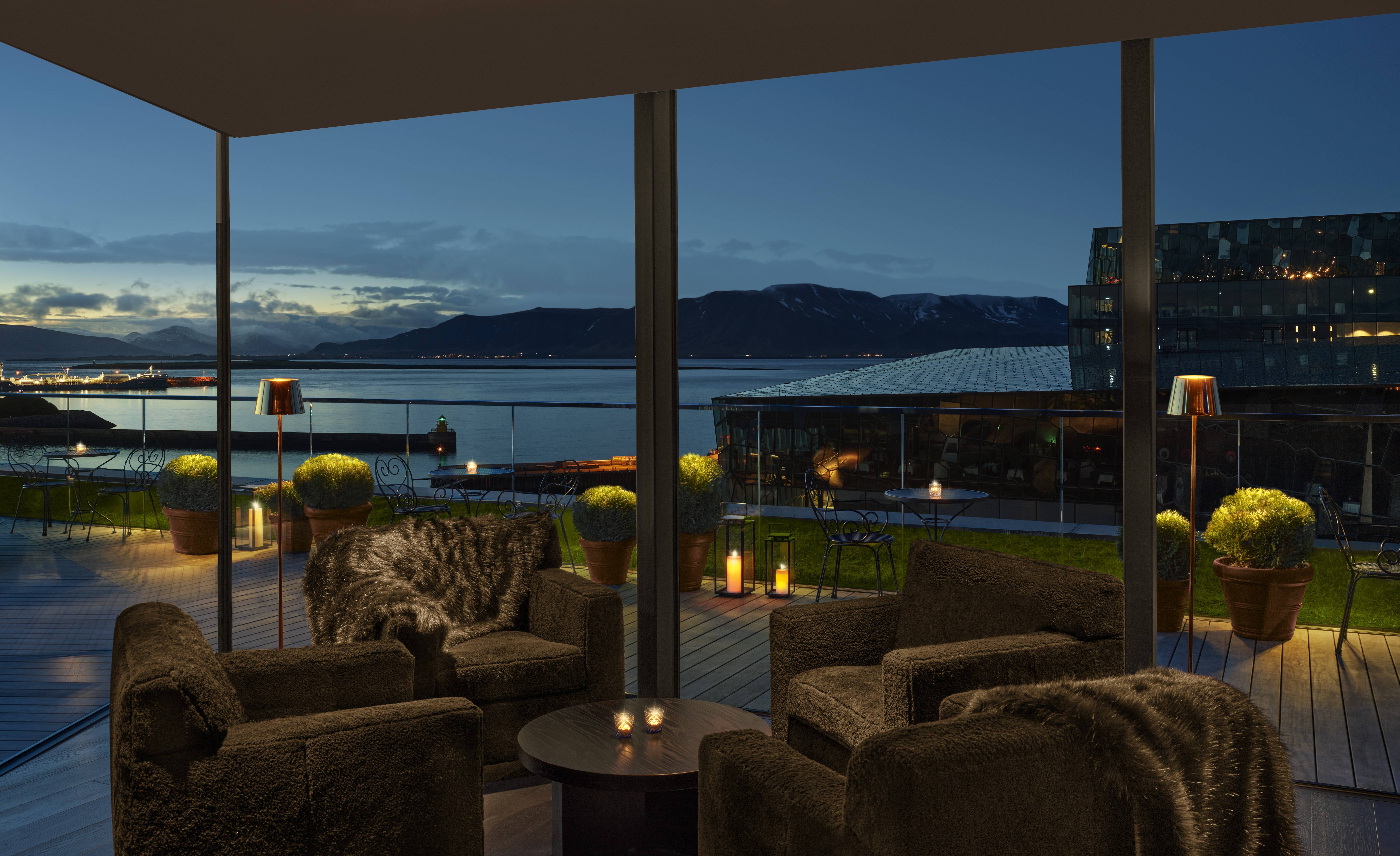 A rooftop at night with warm candle lighting and ocean and mountain views