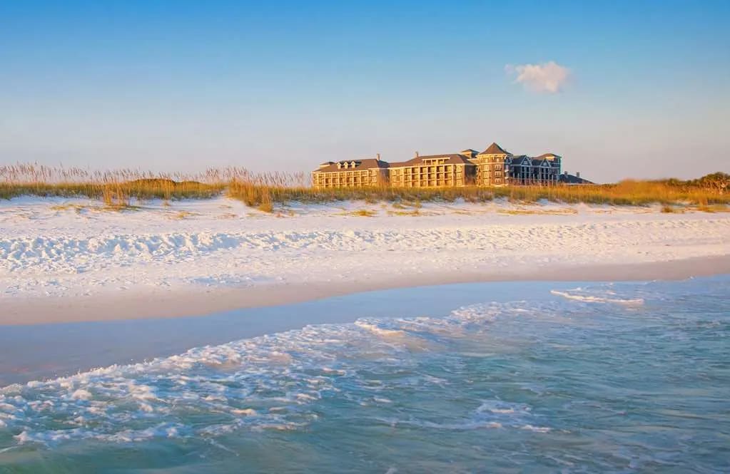 waves gently coming onto a white sand beach with a hotel on the sand dune in the background during day