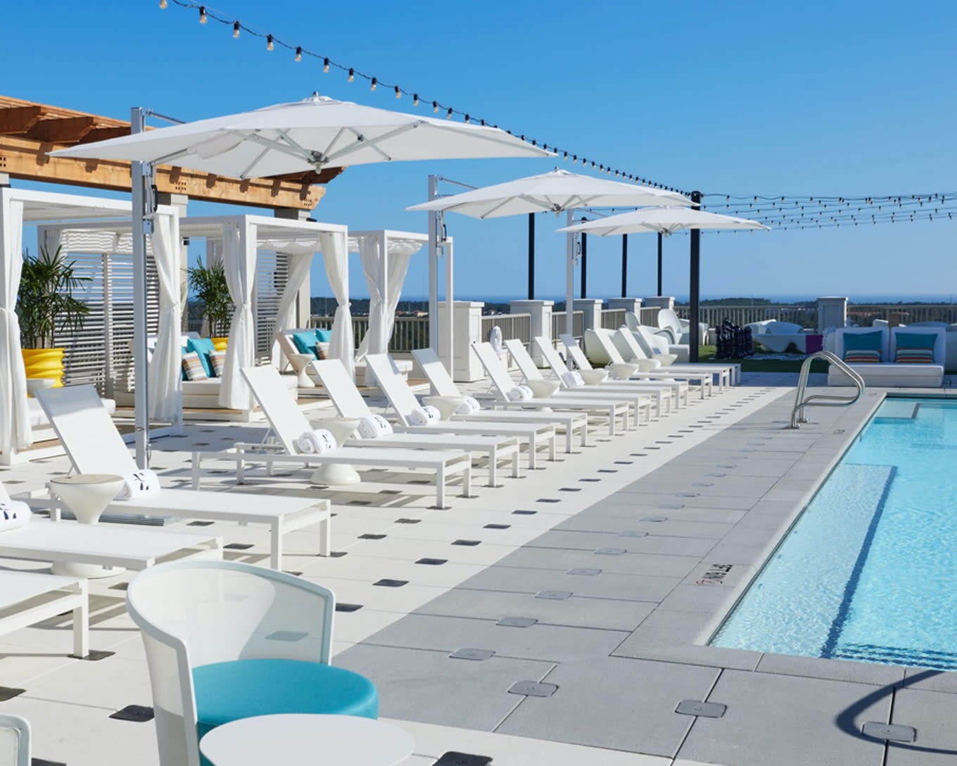 rooftop pool lined with white lounge chairs and umbrellas during day