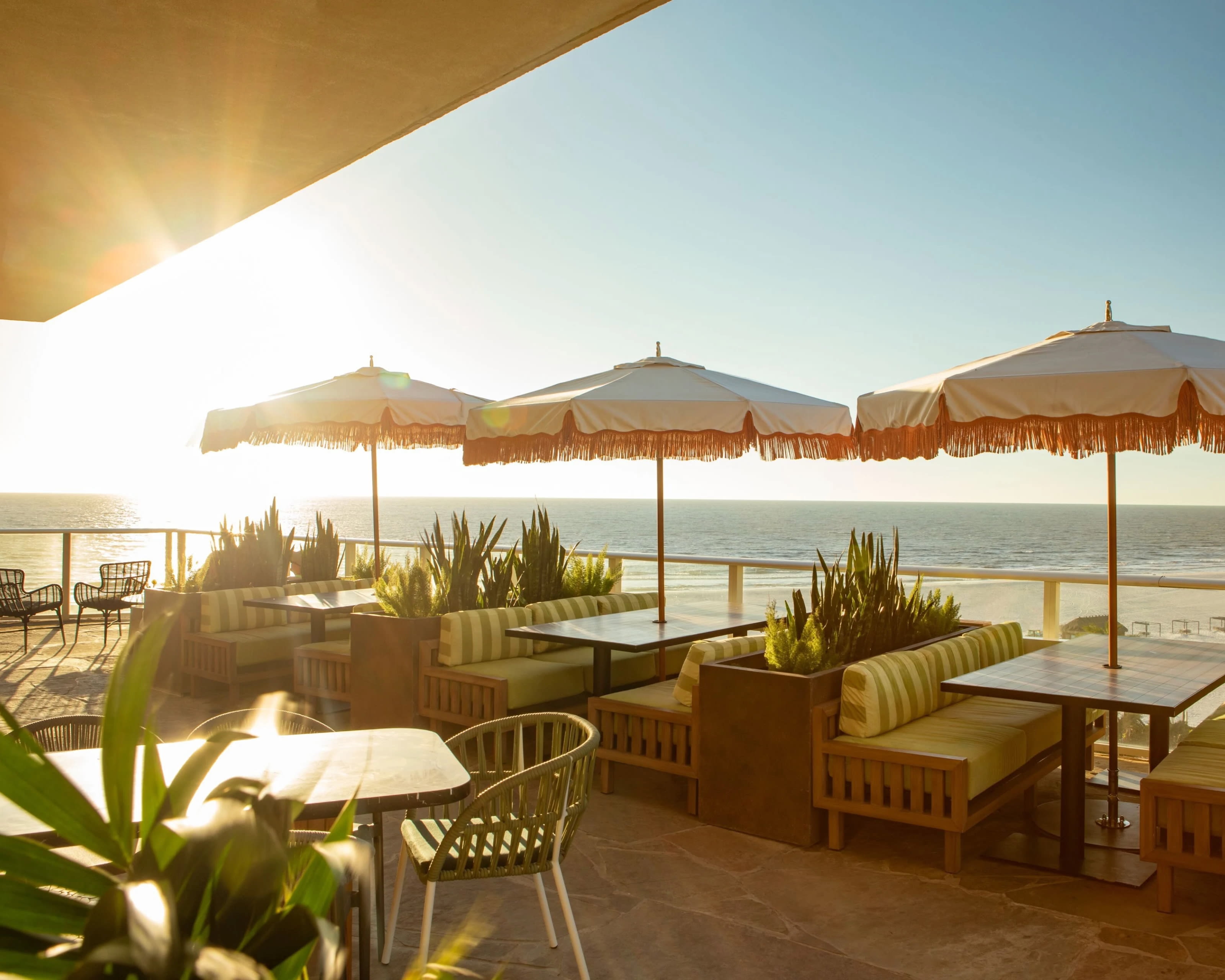 restaurant booths, tables and umbrellas with beach and ocean in the background and the sun shining
