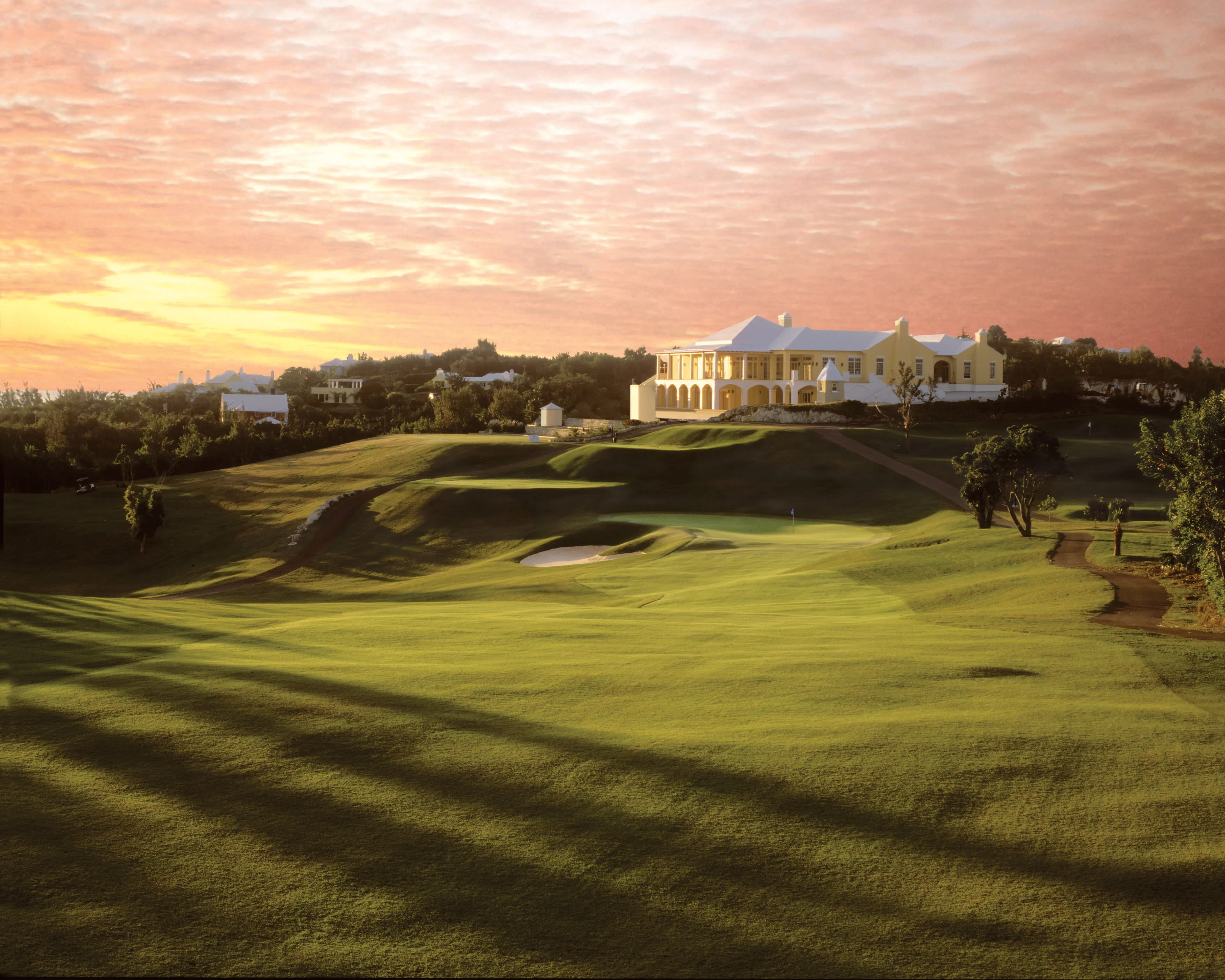 green golf course at sunset with a white golf club building on top of a hill