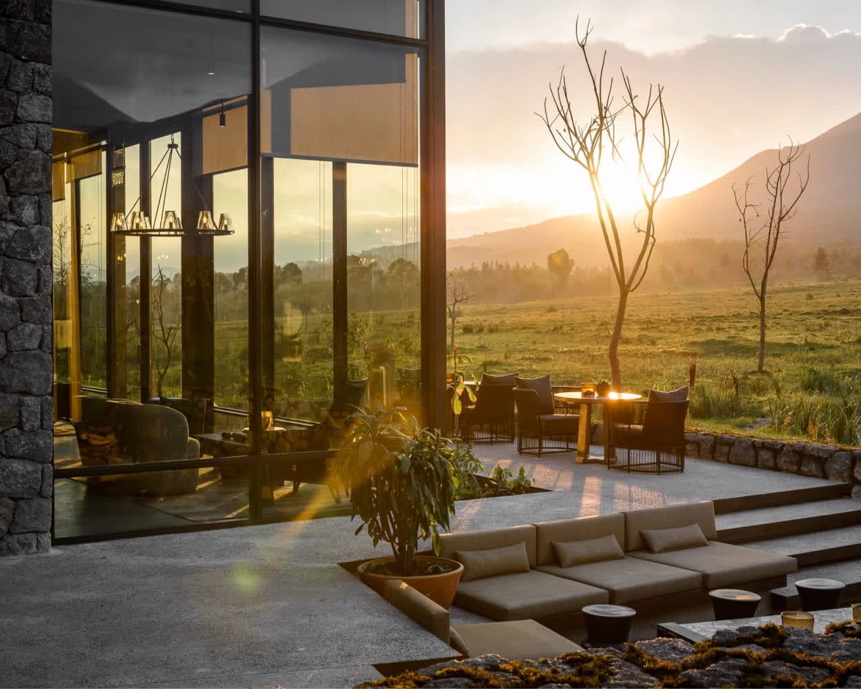 patio with chairs and seating modern outside of a lodge with stone, glass and metal as the sun sets over the mountains in the distance