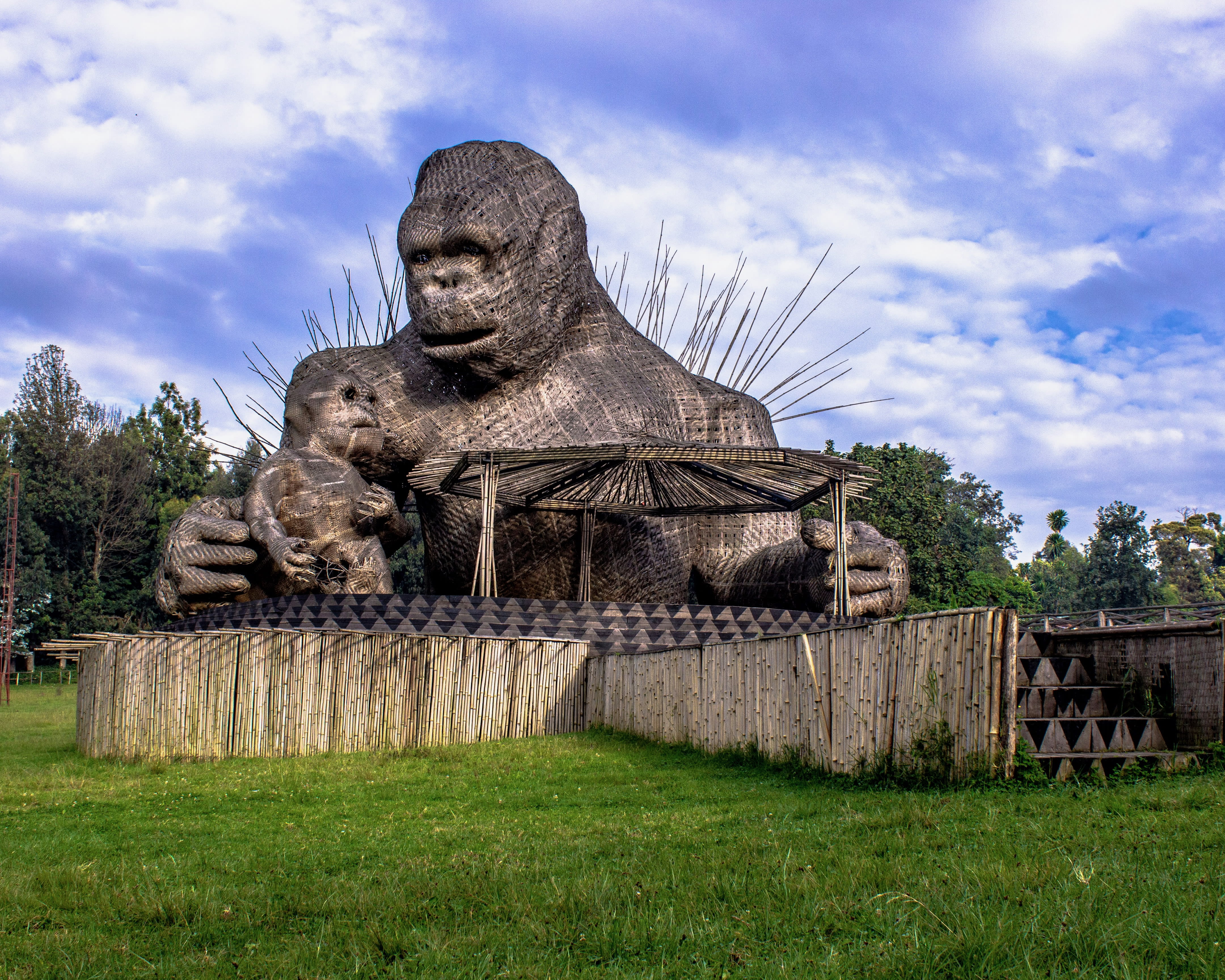 a wooden gorilla and baby gorilla monument with green grass and blue sky