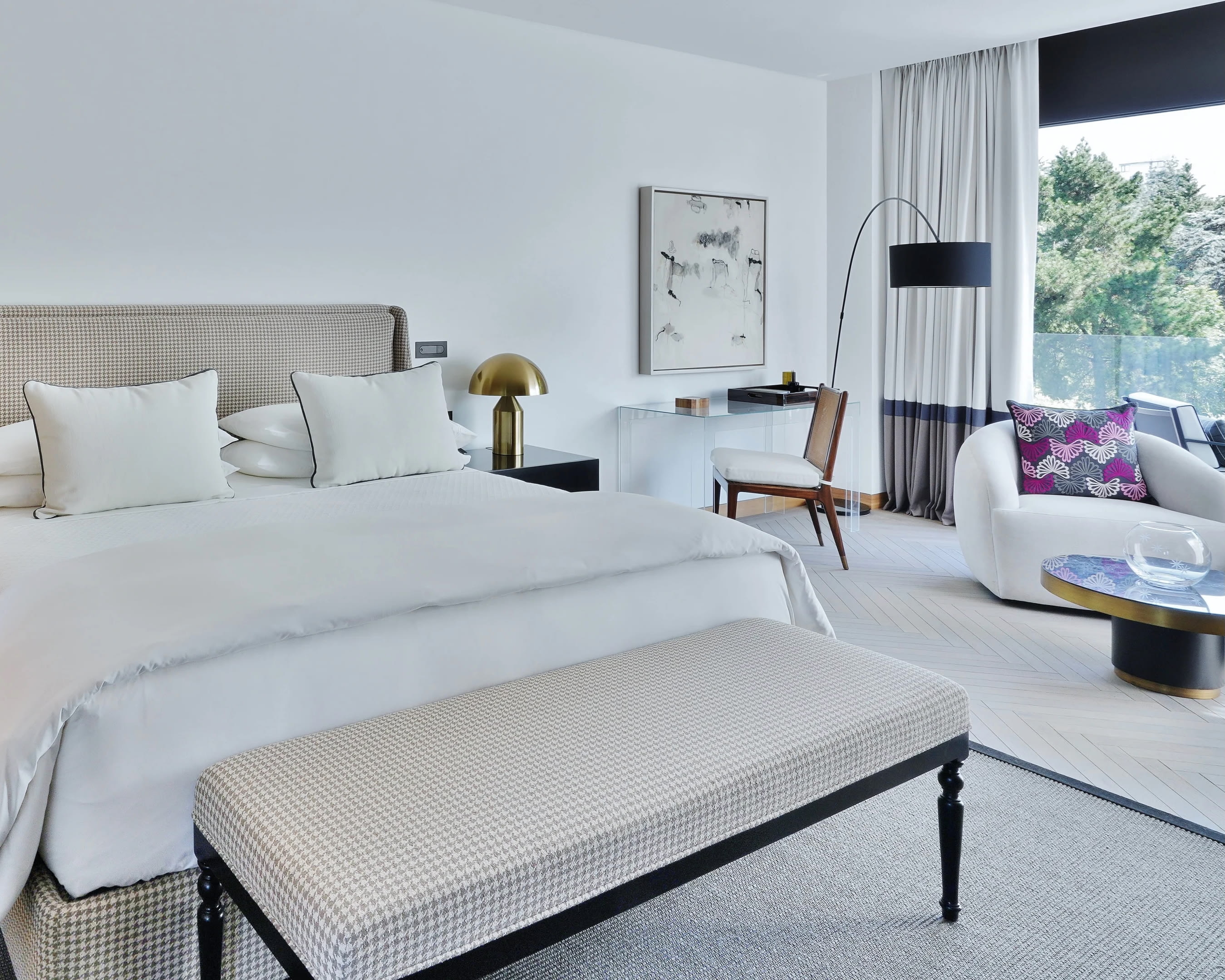 White hotel room with bed, chair, and seating area and gold, purple and black accents