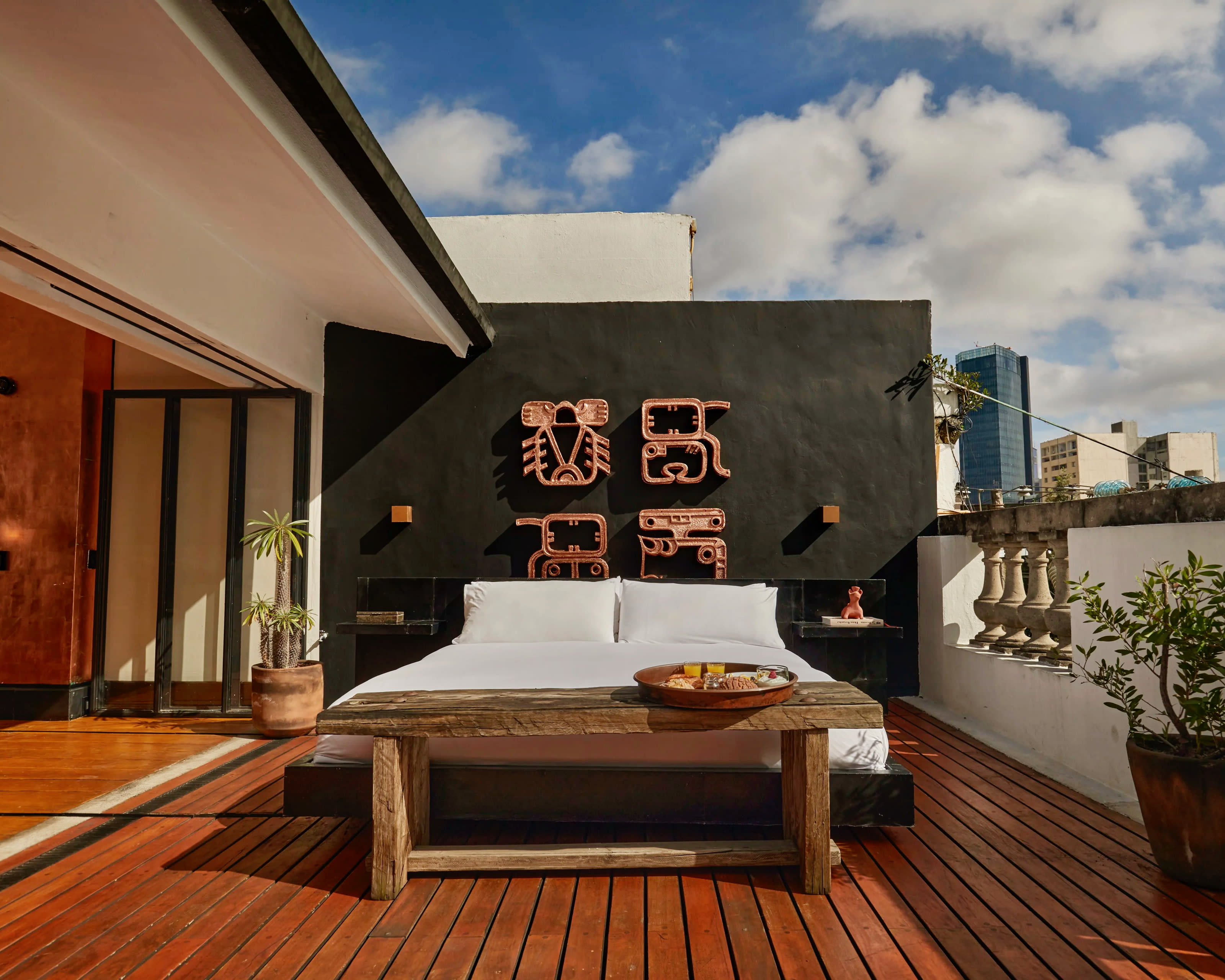 outdoor patio with wood decking, black wall, artwork, and a white linen covered bed outside during day