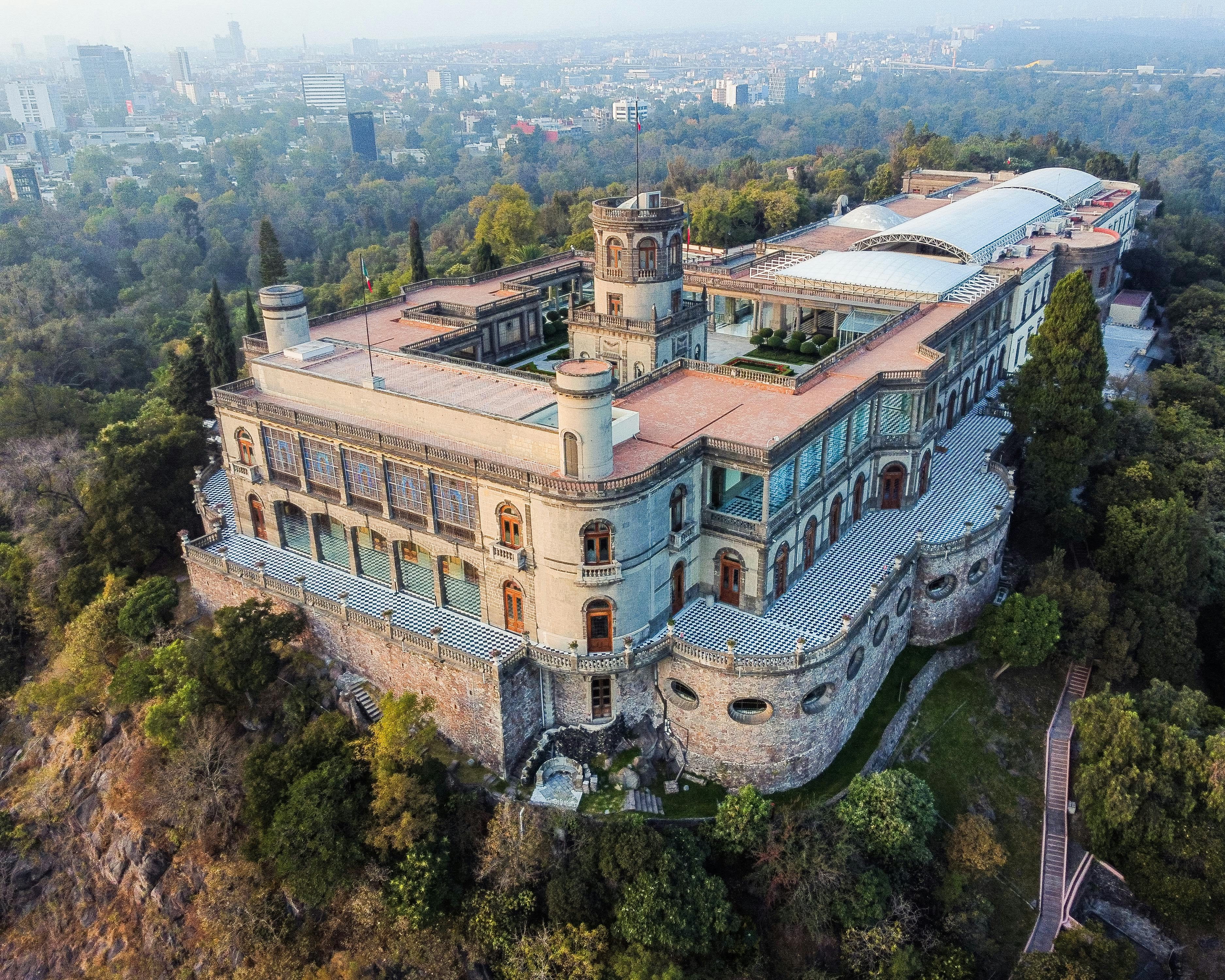 aerial view of hilltop castle with green trees and city in the background during day