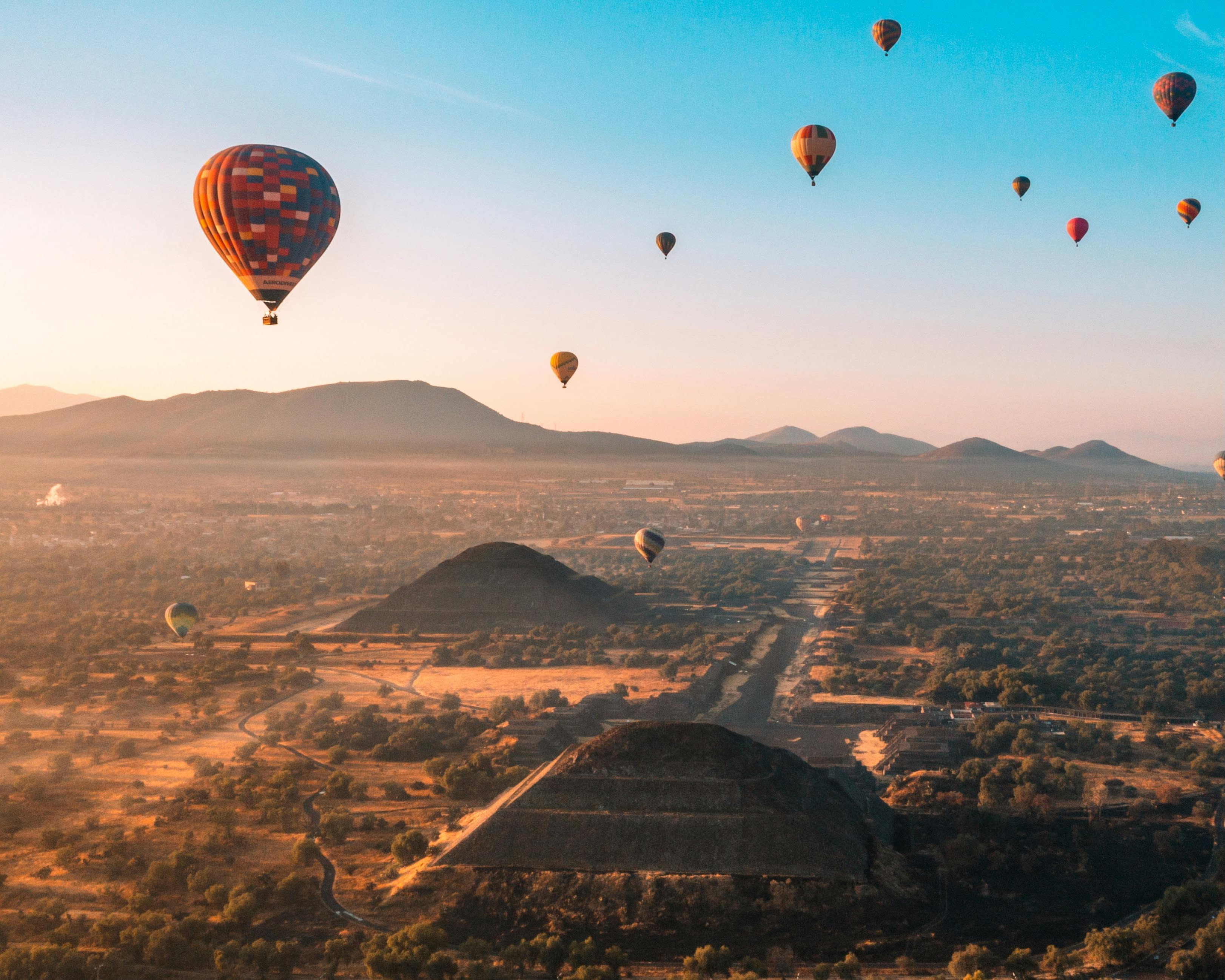 aerial view of hot air balloons above pyramids during sunrise