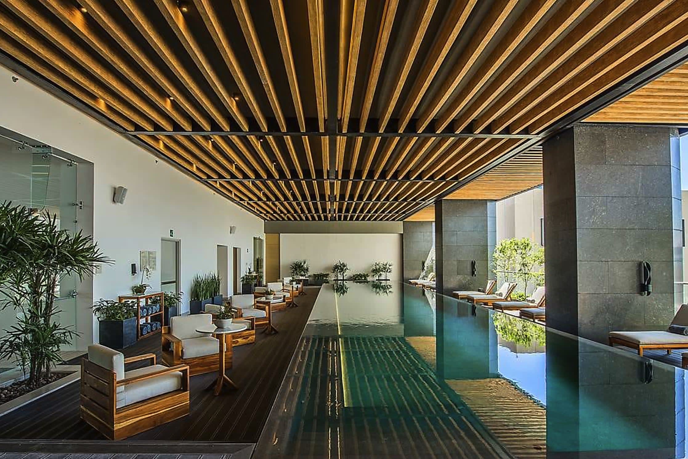 A stylish, covered hotel pool area with a wood-paneled roof, neutral, modern furniture and a view.