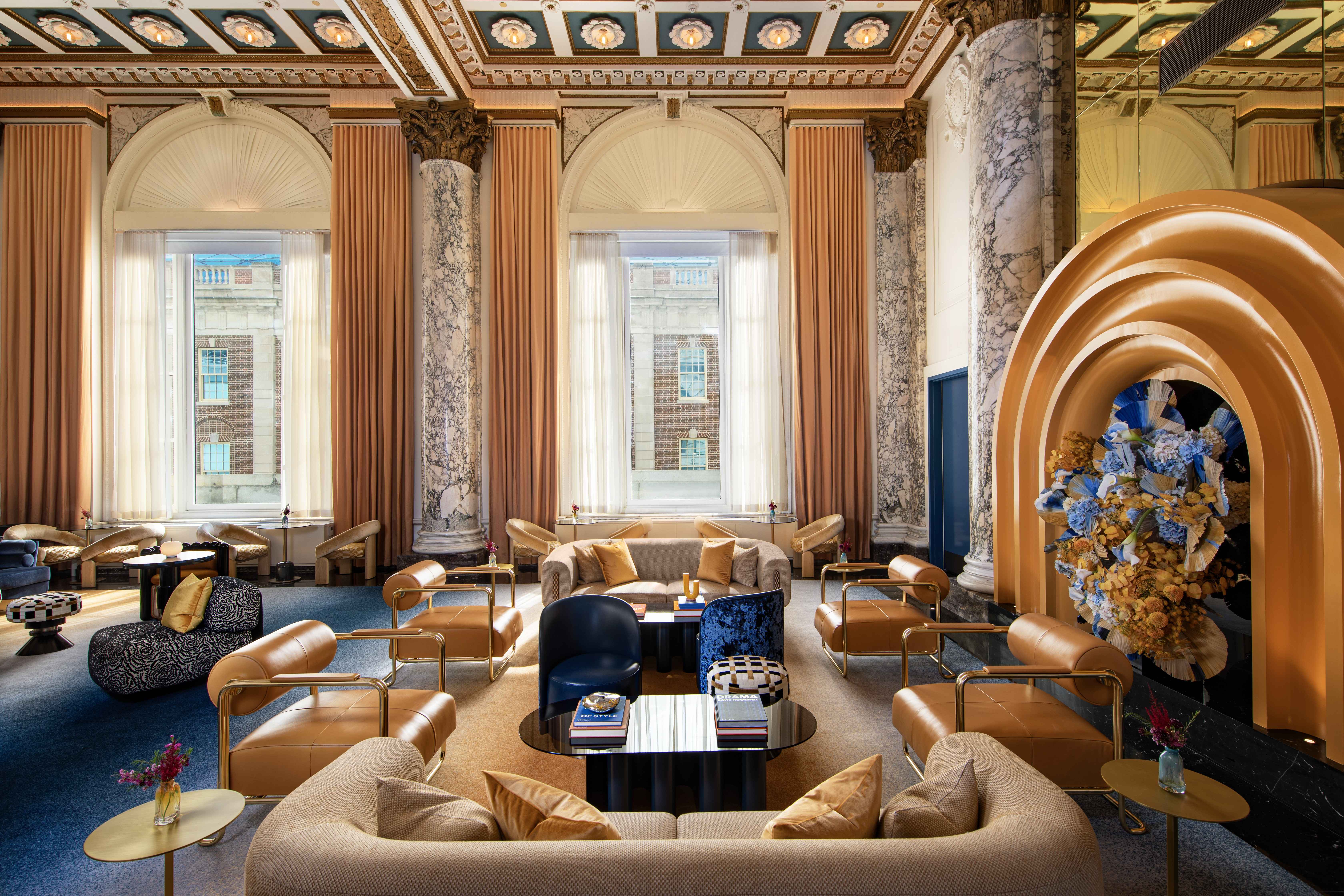 Grand hotel lounge with marble columns, arched windows, plush seating, and a striking golden arch adorned with floral arrangements.