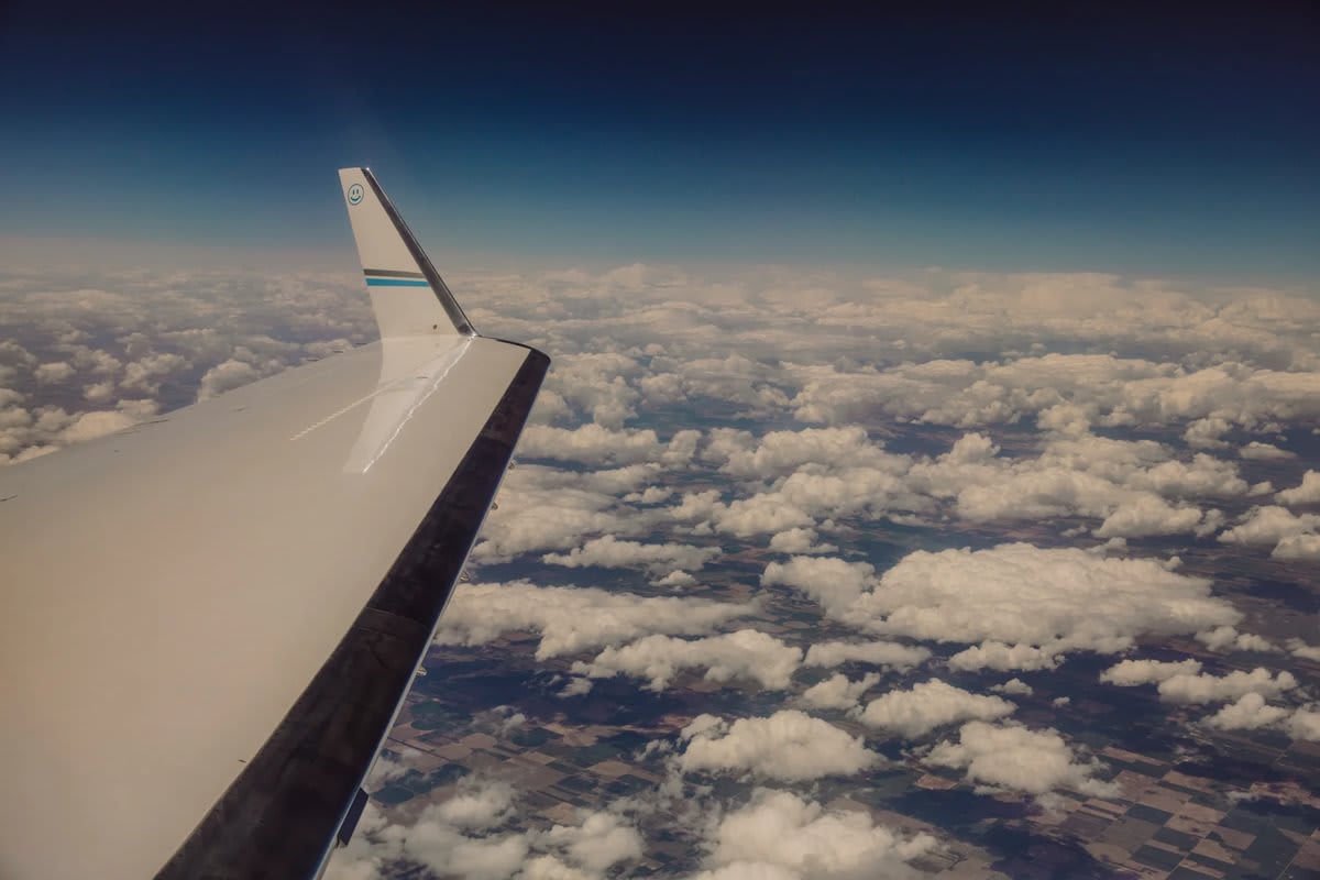 looking out an airplane window with an airplane wing and sky with clouds