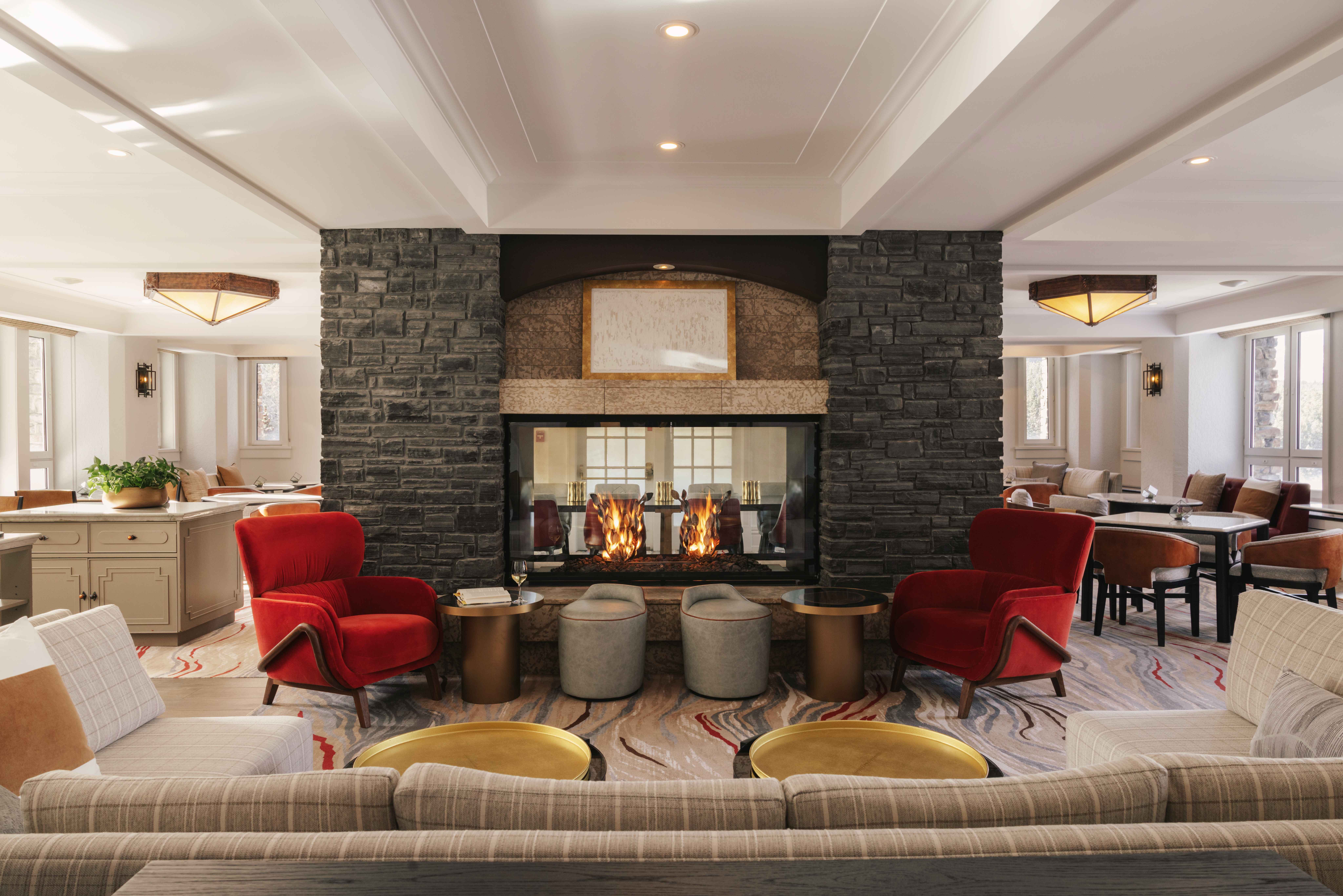 Modern hotel lounge with a double-sided stone fireplace, red velvet chairs, and cozy seating areas.