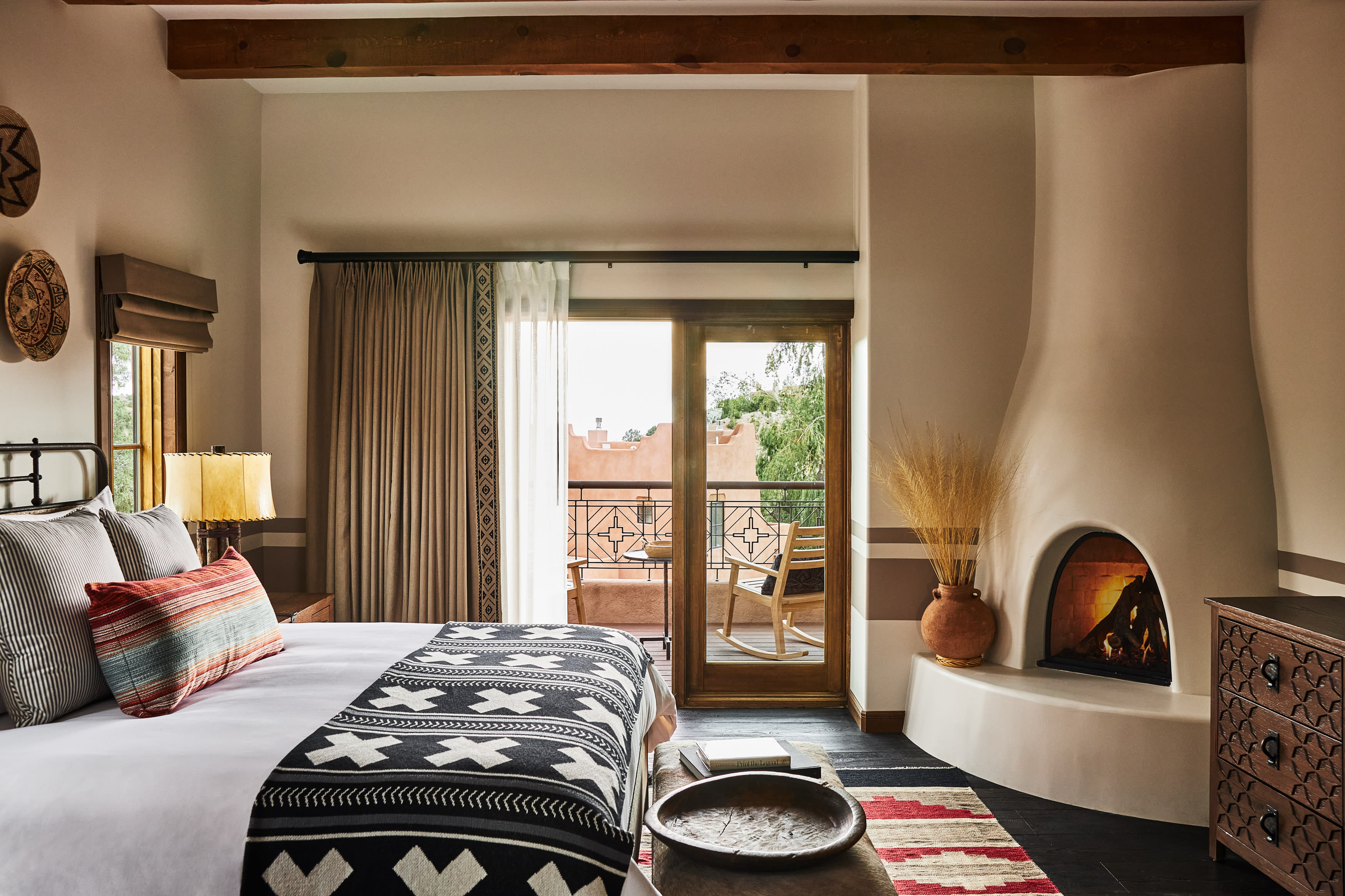 Southwestern-style suite with a kiva fireplace, rustic wood ceiling, patterned textiles, and a terrace overlooking desert hills.