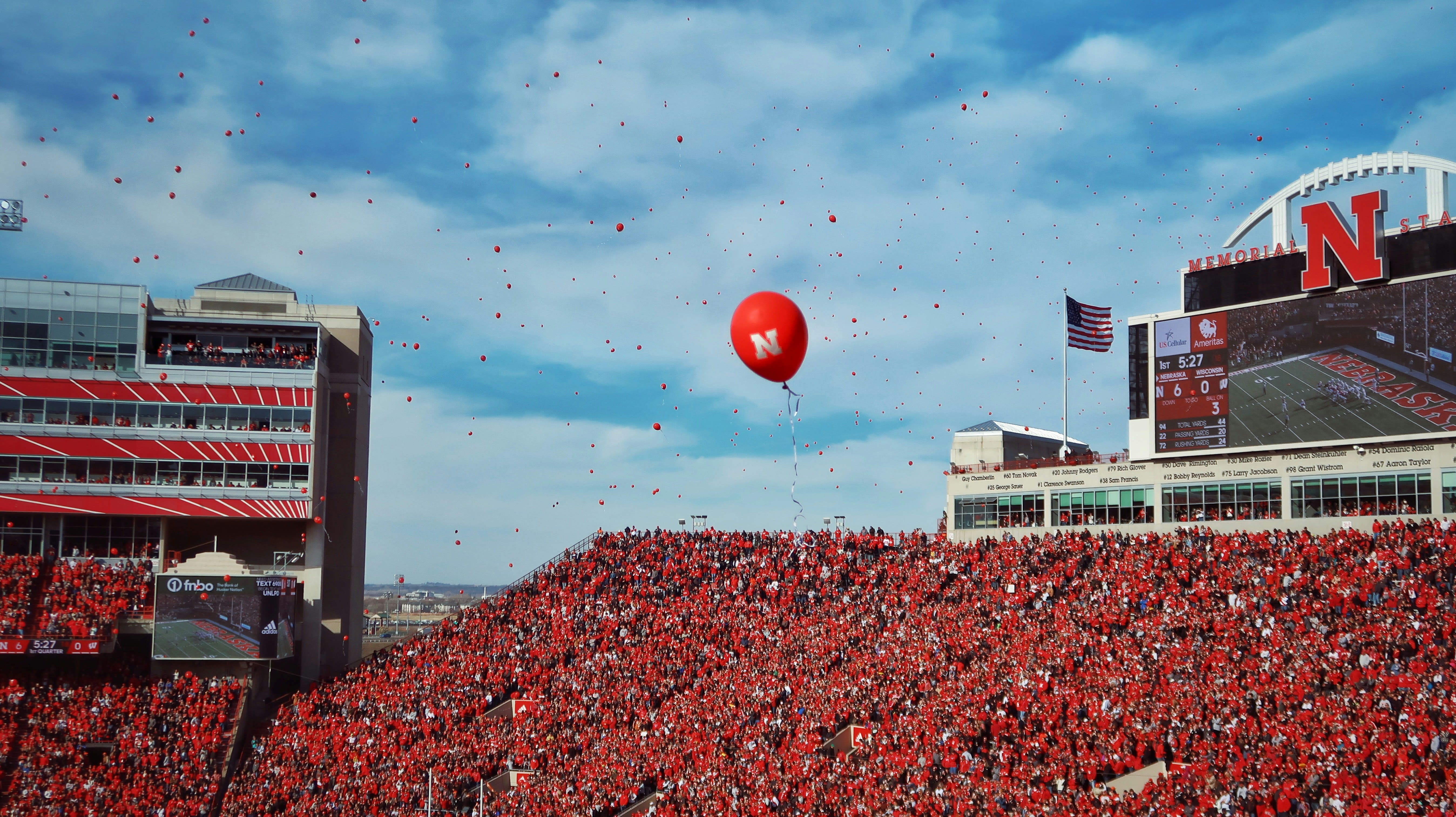 outdoor stadium with a bunch of red balloons floating in a blue sky