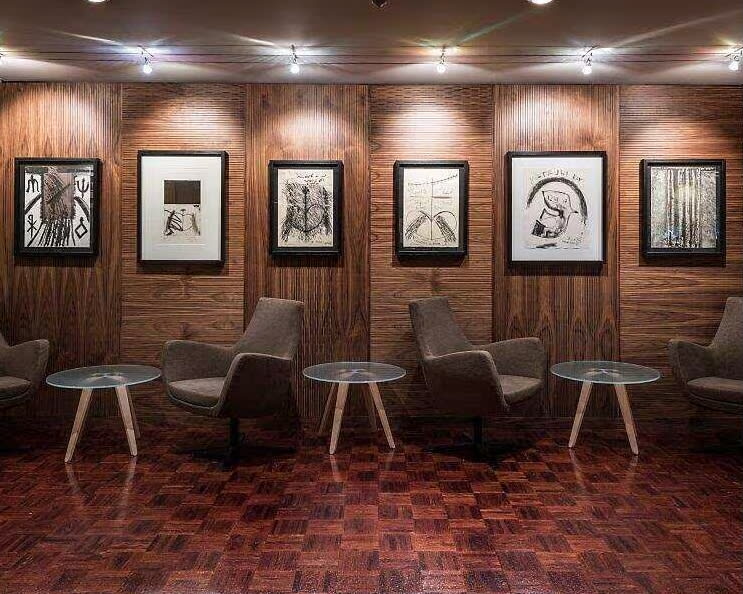 brown wood wall of illuminated artwork with side tables and chairs under