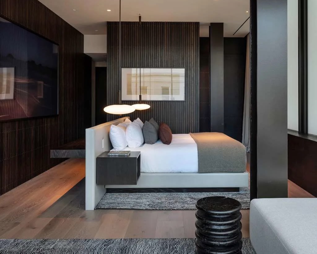 side view of modern grey hotel room with bed covered in white linens and maroon accent pillow