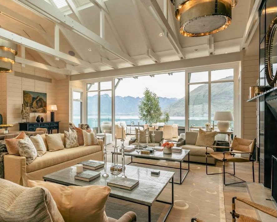 contemporary villa living room with cream colored furniture, glass tables, wood beam ceiling, and mountains and lake outside