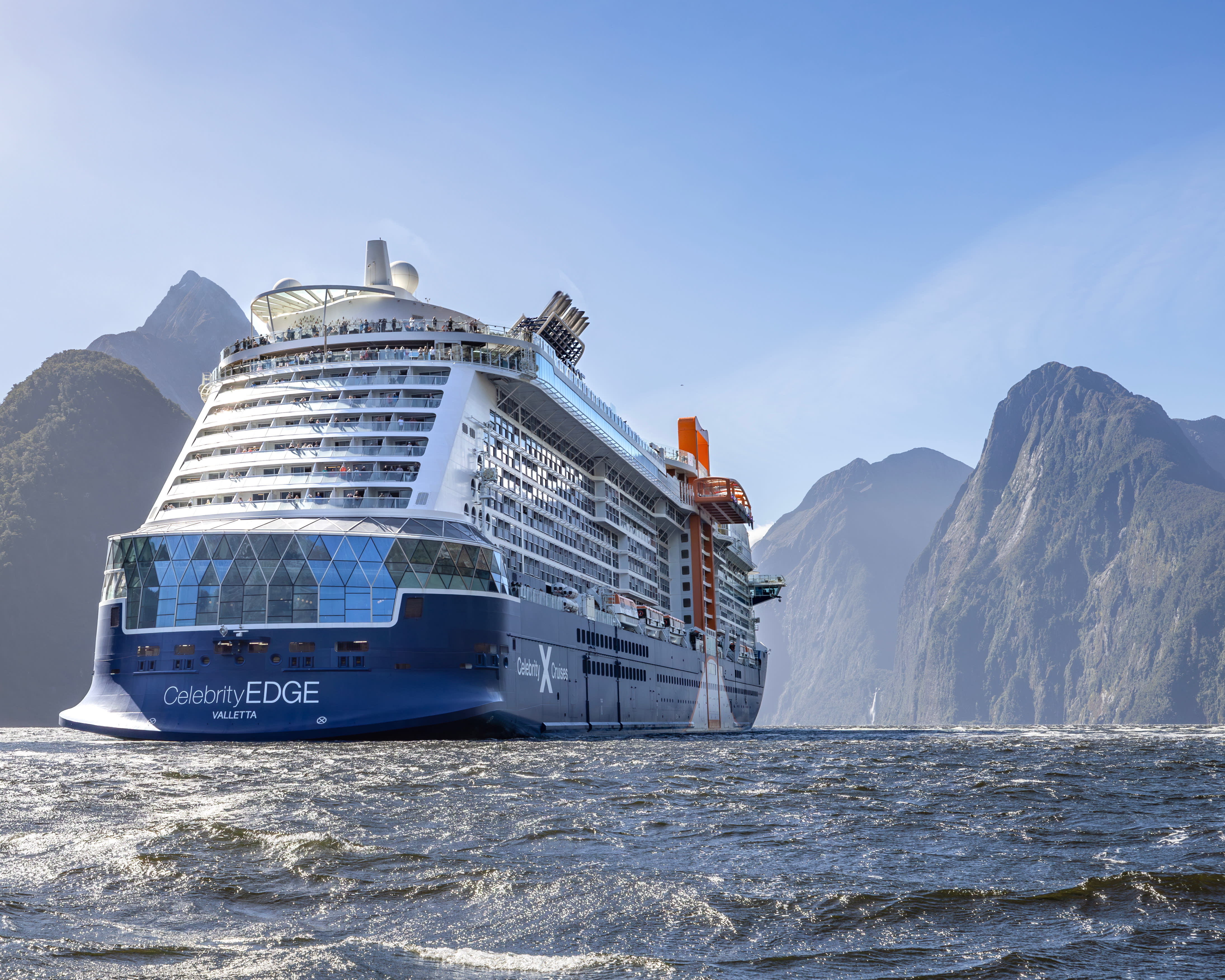 large modern cruise ship on choppy waters during day sailing into a green fjord
