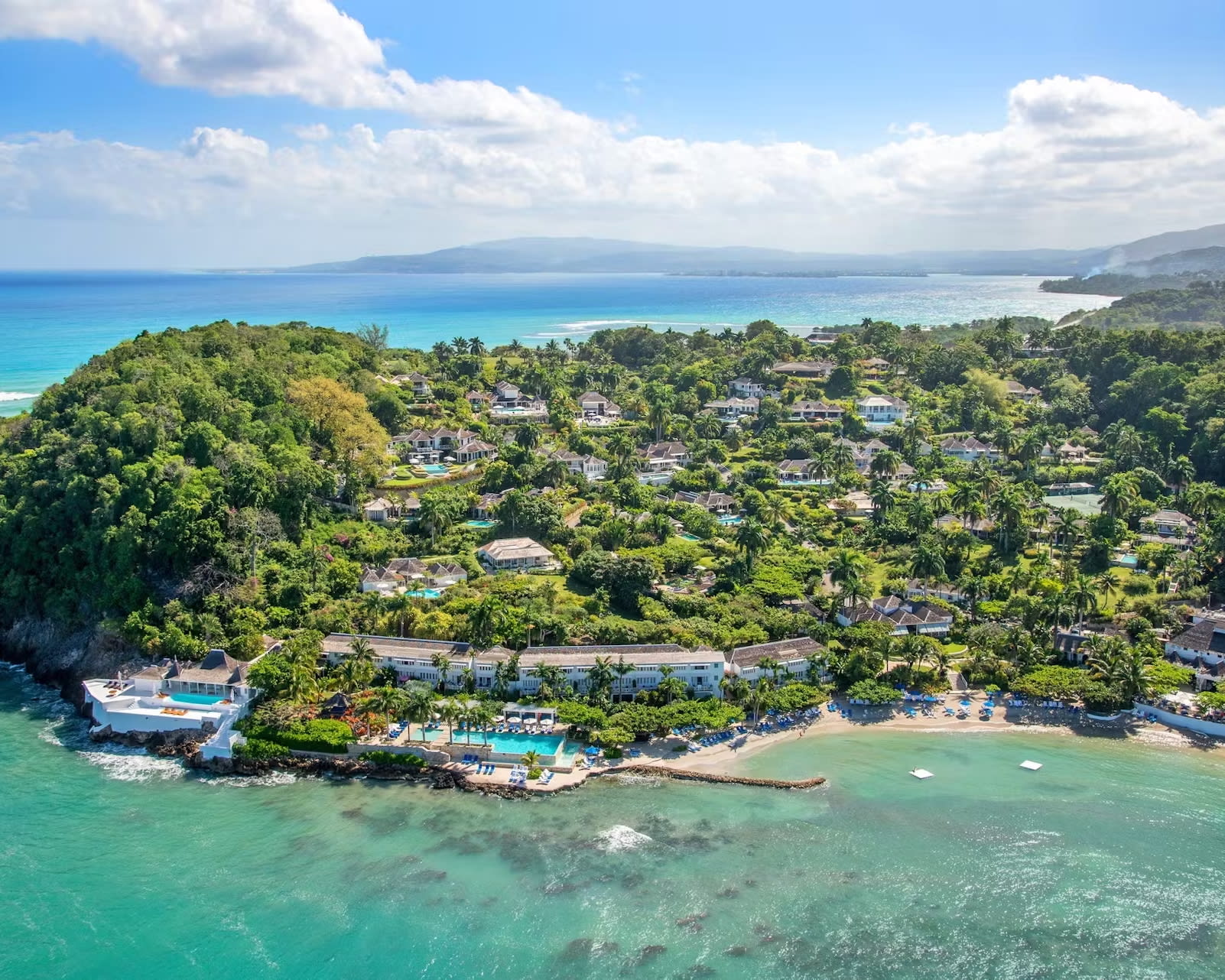 aerial view of hillside hotel estate with villas and cottages above turquoise waters during day