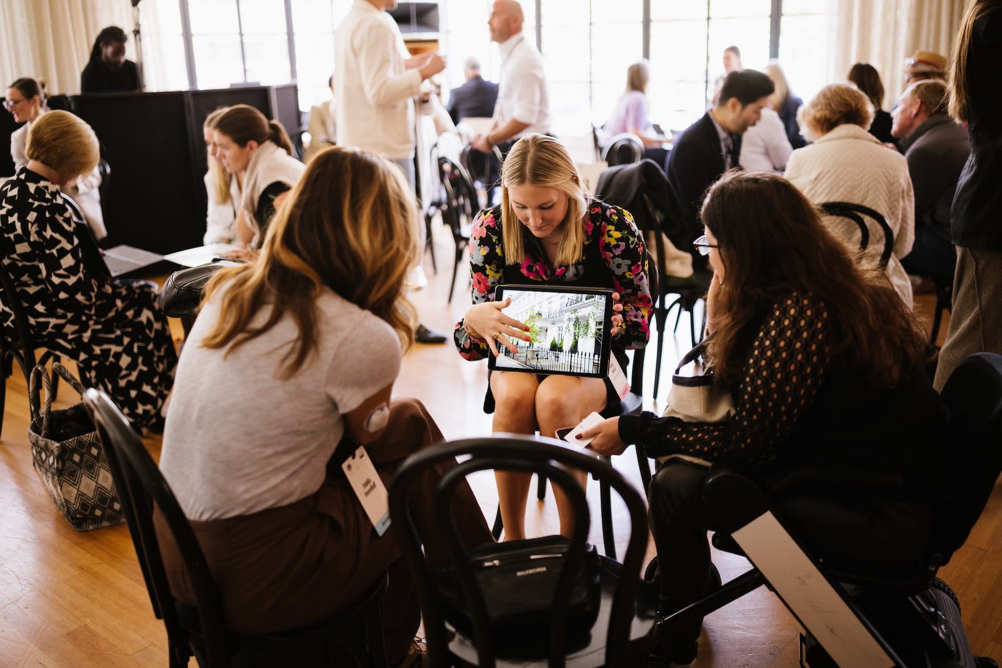 Small group of people seated in a workshop, with one woman showing a hotel image on her tablet during a collaborative travel advisor session.