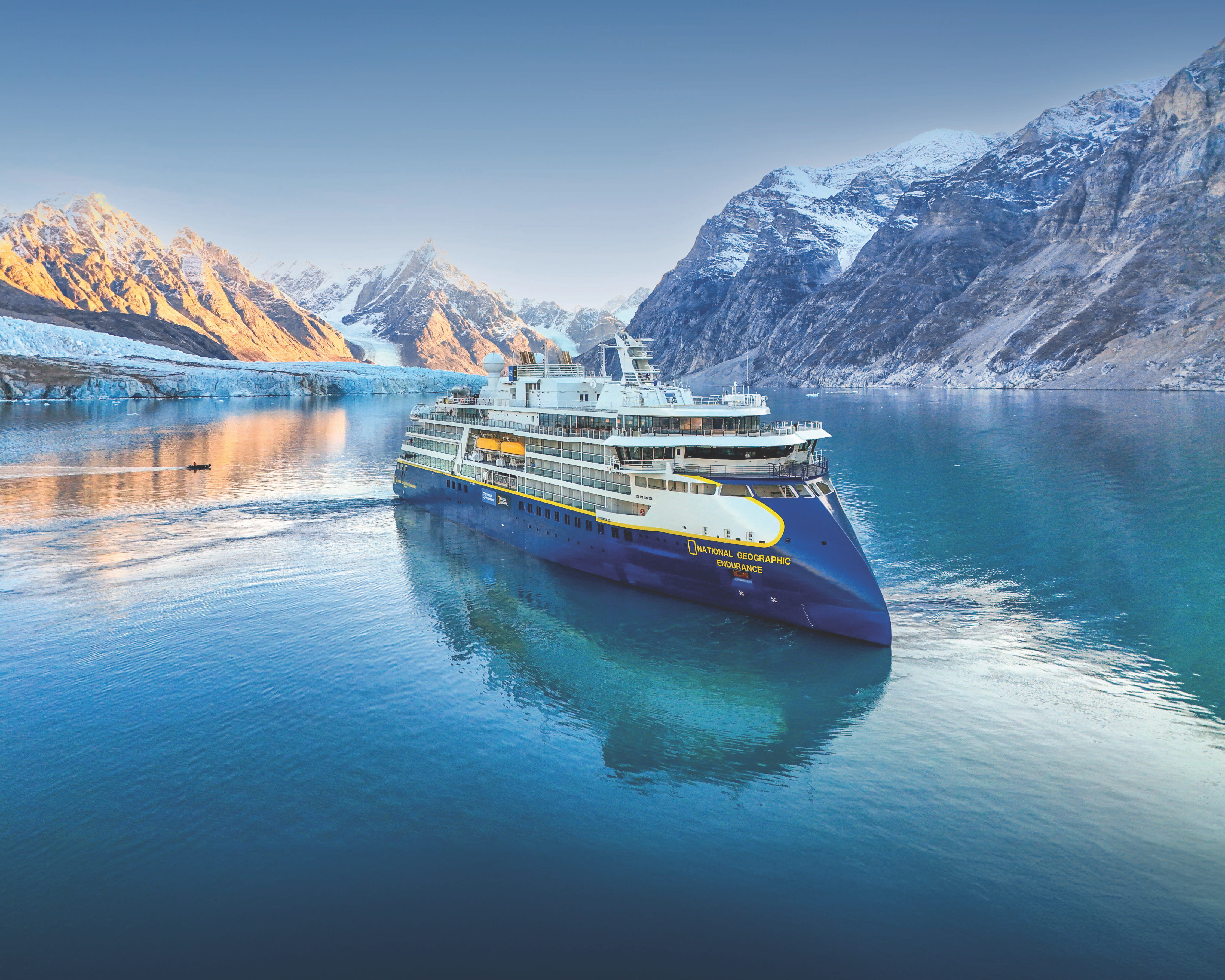 A small expedition ship in icy turquoise waters with snow capped mountains in the background during day