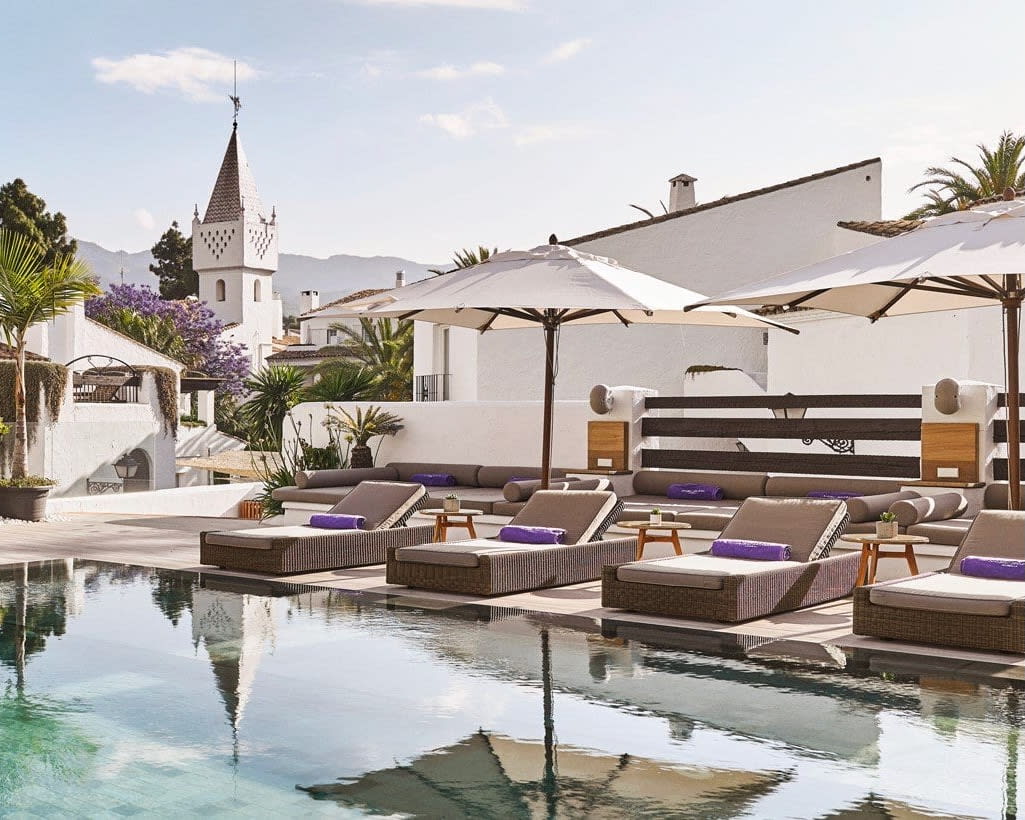 pool with grey sun loungers and white umbrellas with a cityscape in the background during day