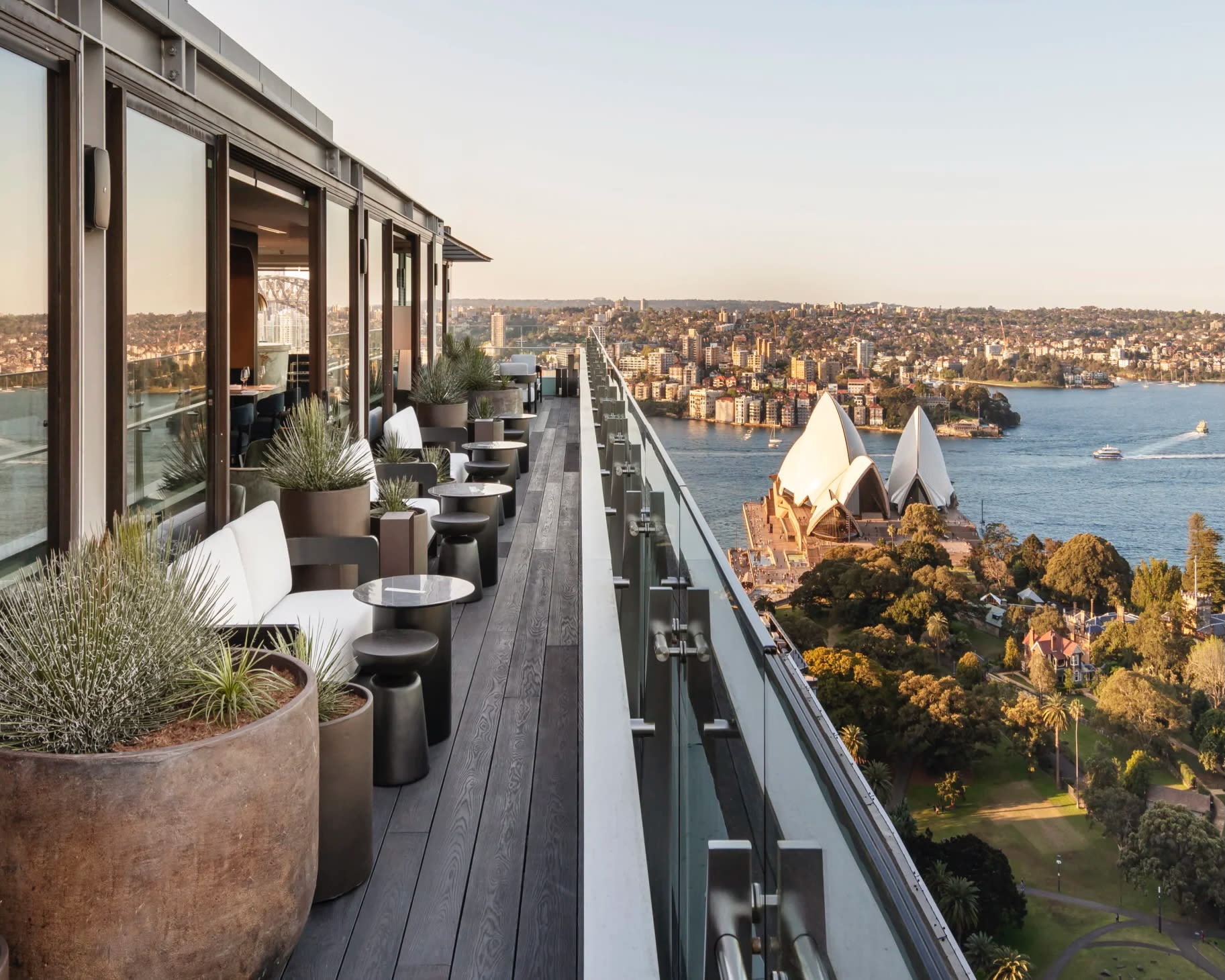 A rooftop terrace lined with white chairs overlooking harbor and cityscape during day