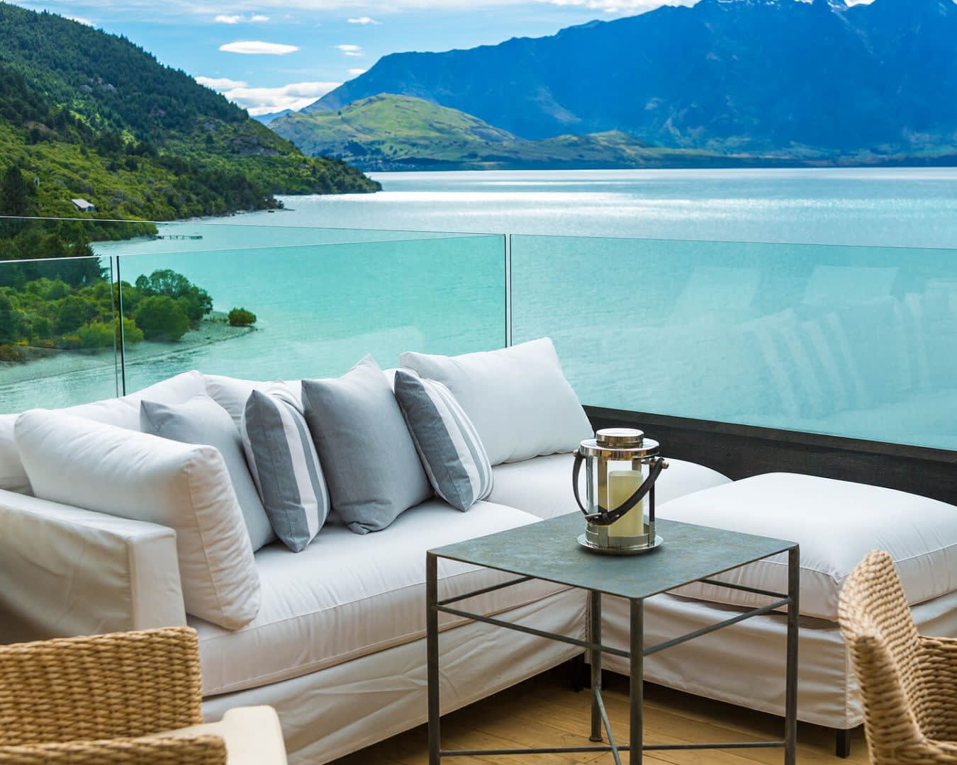 White sofa on glass walled balcony overlooking a lake and green mountains during day