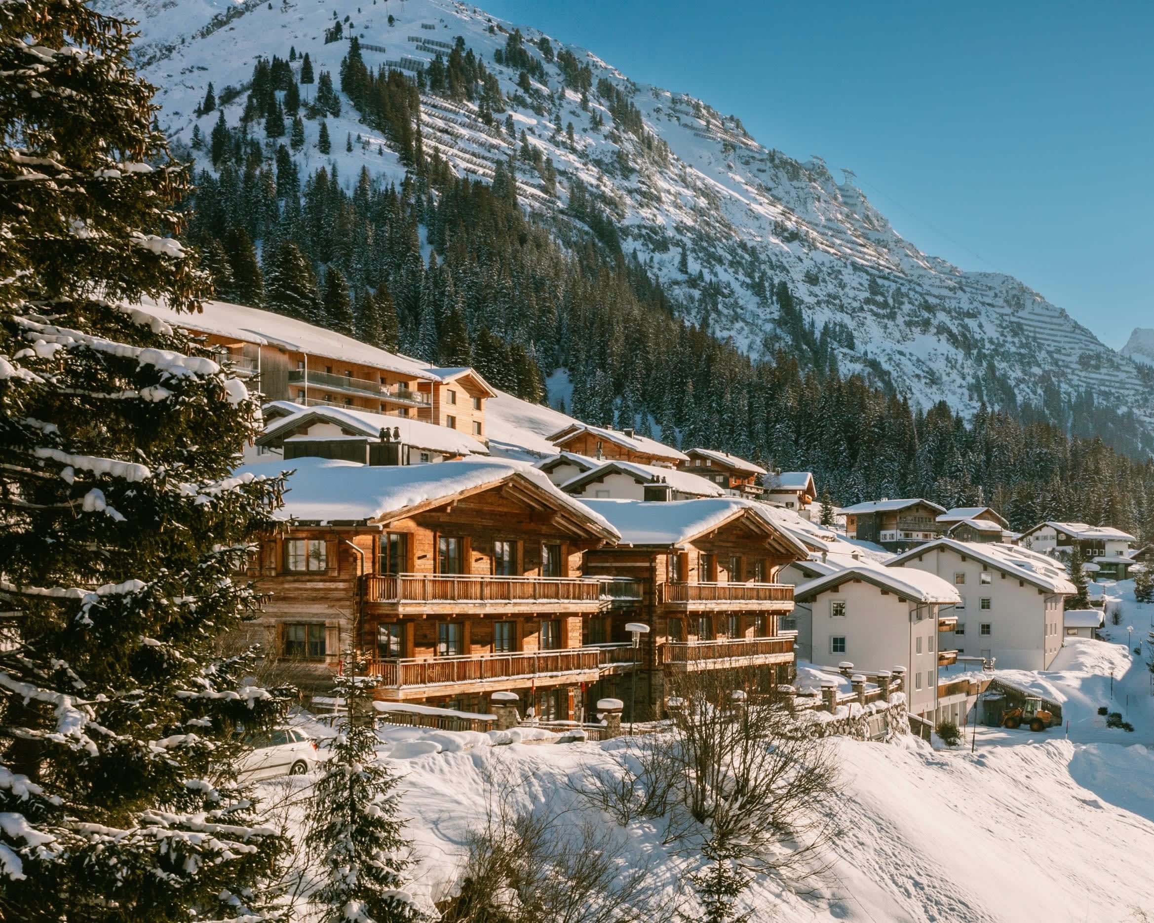 A snowy wooden mountain lodge on the side of a hill with mountains behind during day