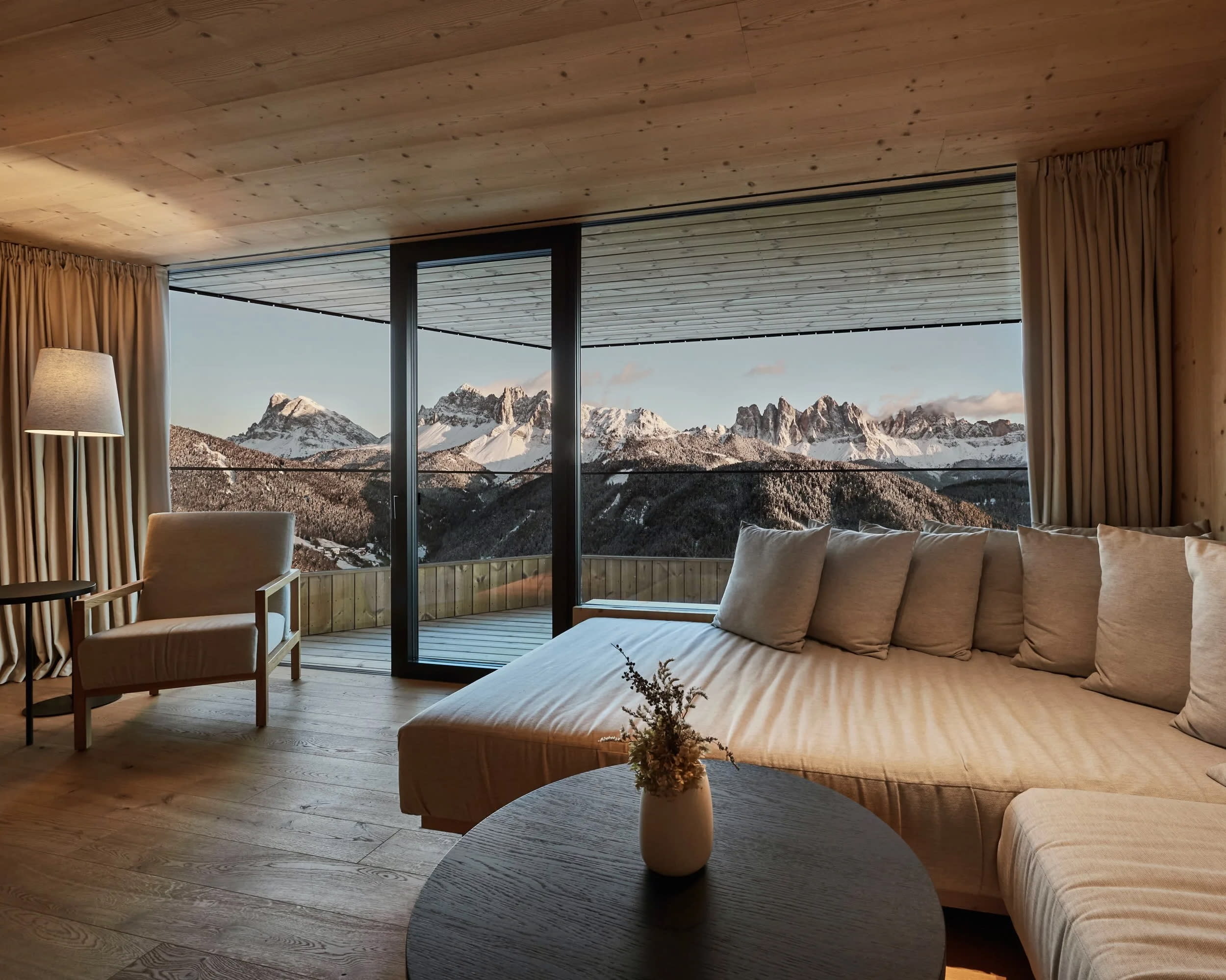 living room sofa and chair with floor-to-ceiling windows and snow covered mountains outside during day