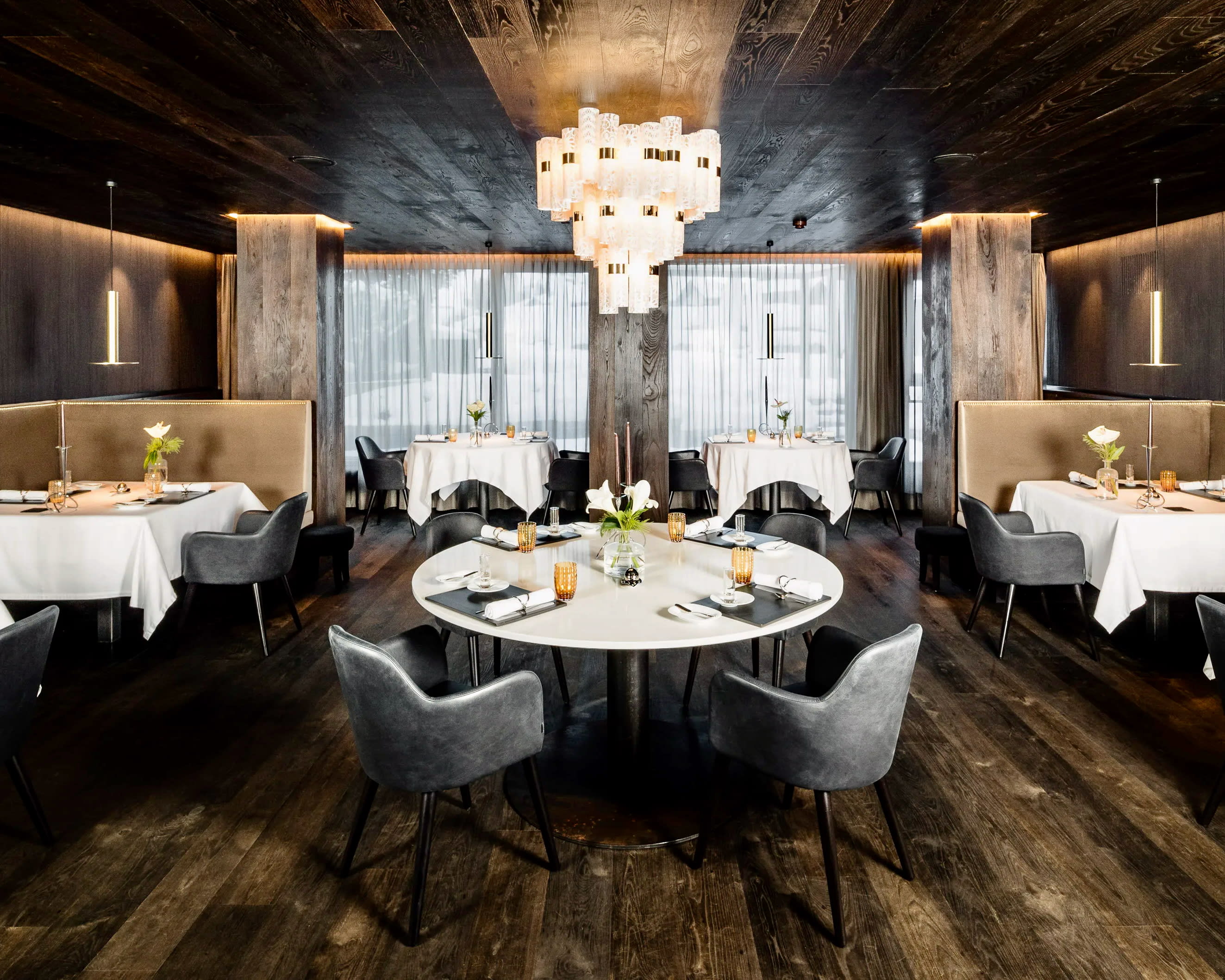 restaurant with white tables, grey chairs, black wood floor and ceiling, and modern chandelier