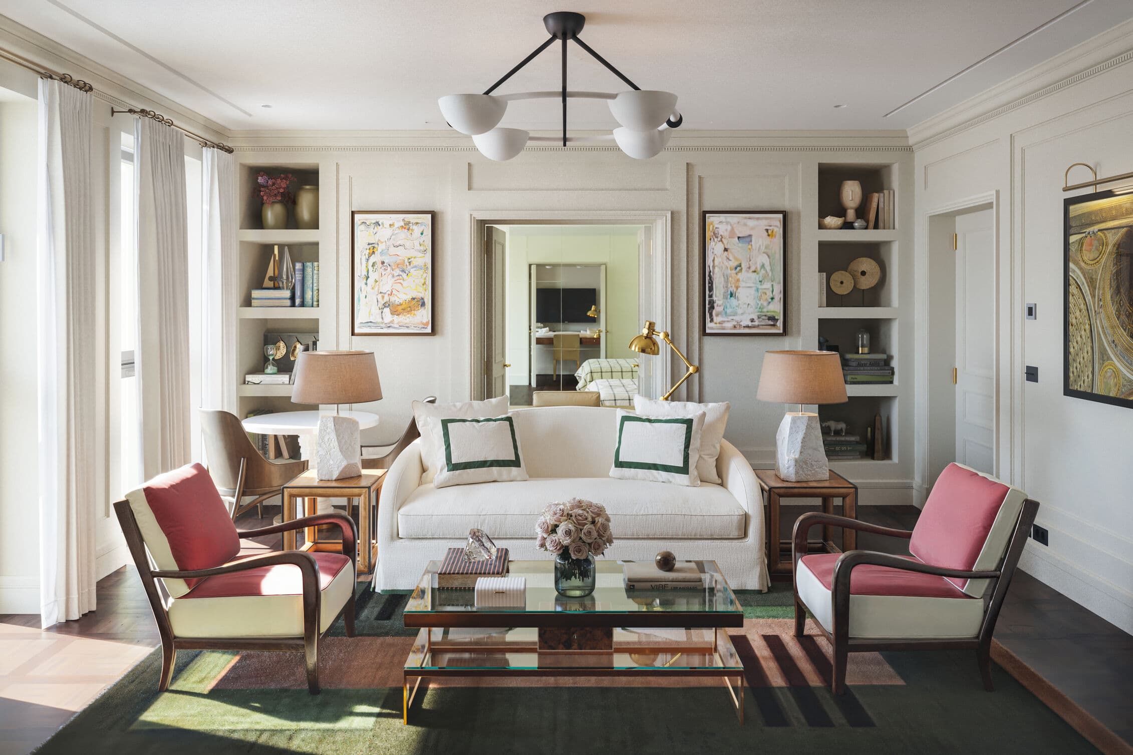 Stylish hotel suite with a cream sofa, red-accented armchairs, and modern art, featuring warm lighting, elegant decor, and a glass coffee table with fresh flowers.