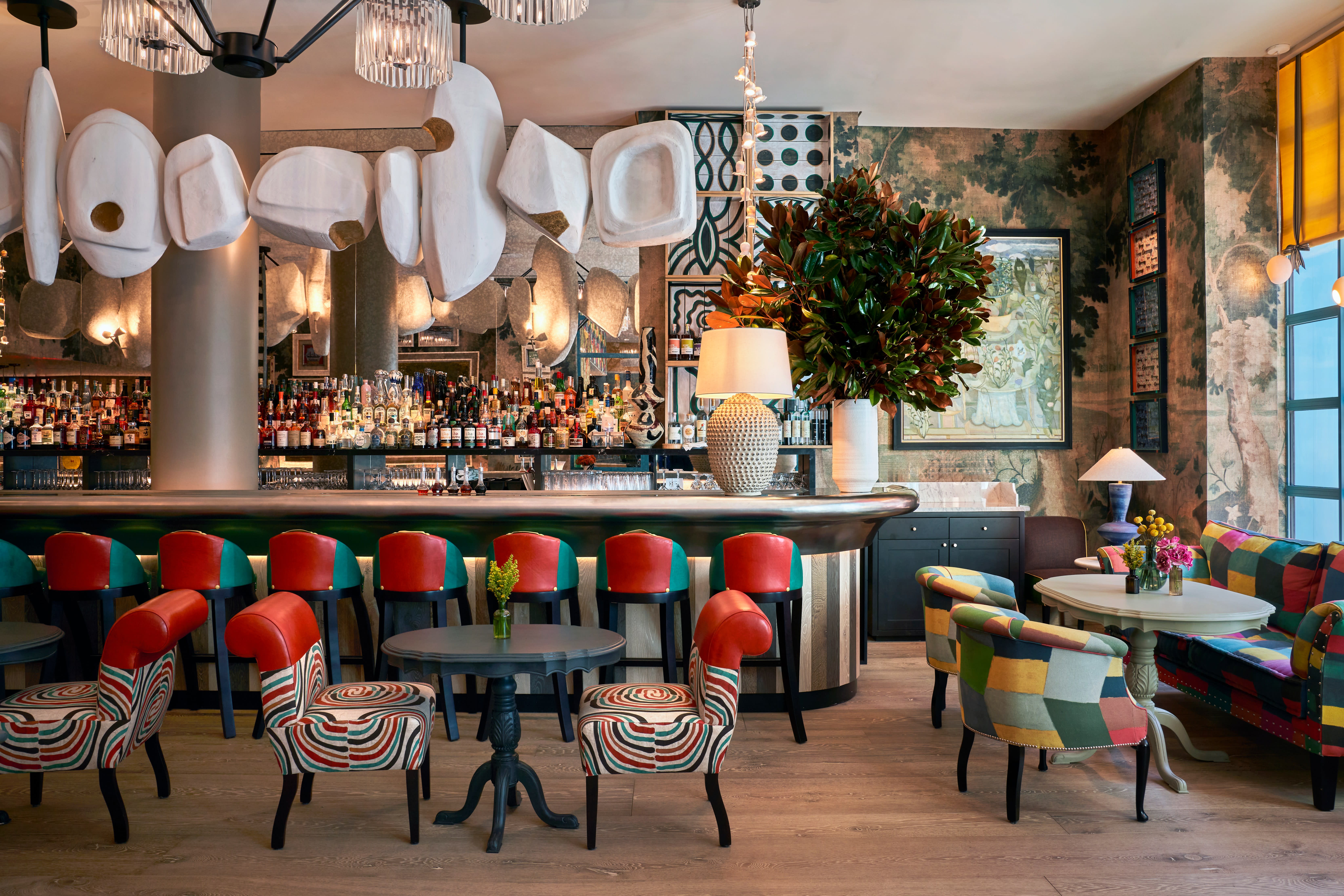 Vibrant hotel bar with eclectic patterned chairs, colorful patchwork seating, and a bold design featuring modern art, lush plants, and a well-stocked bar.
