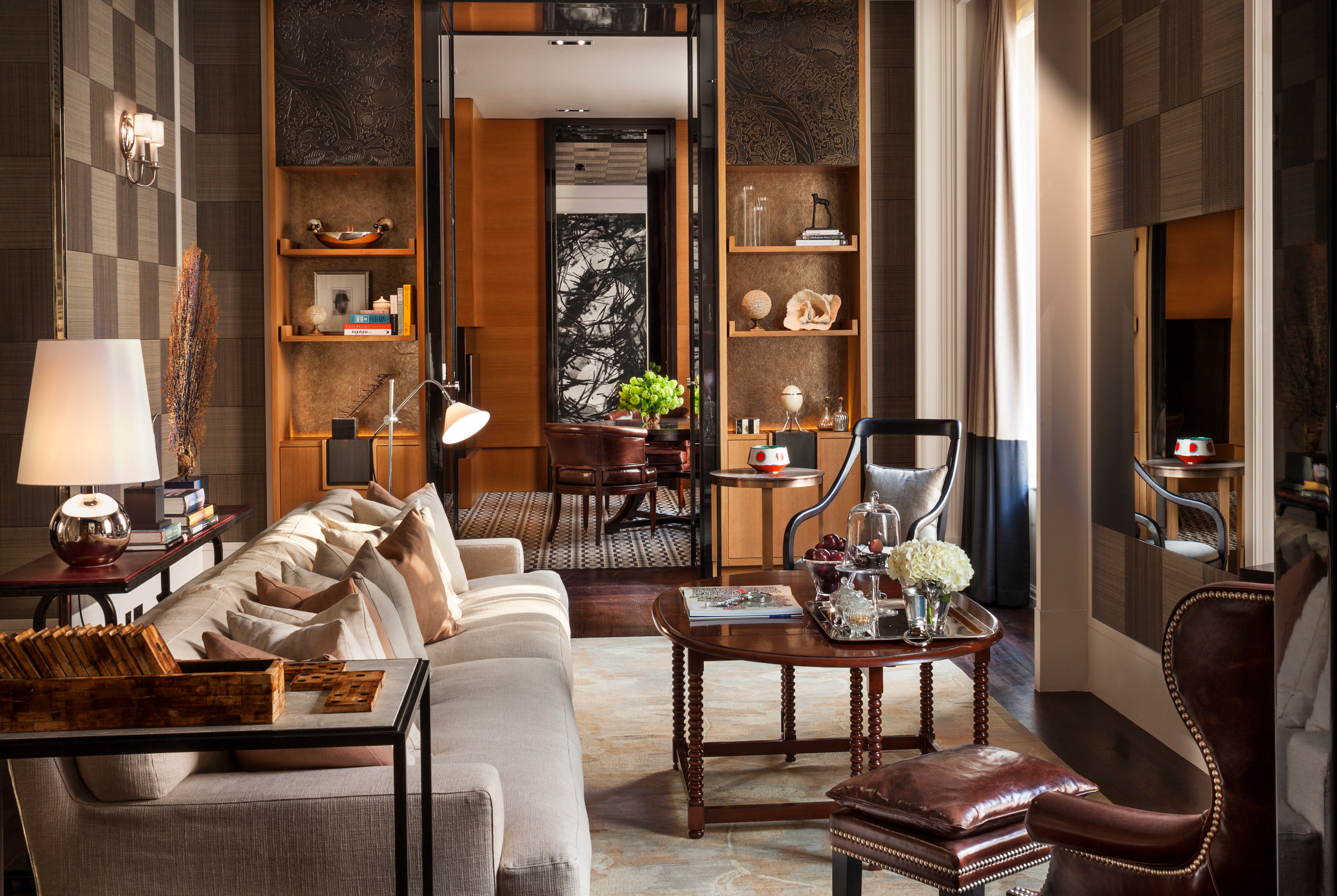Sophisticated living room with neutral tones, plush seating, wood accents, and elegant décor, leading into a study with leather chairs and soft lighting.