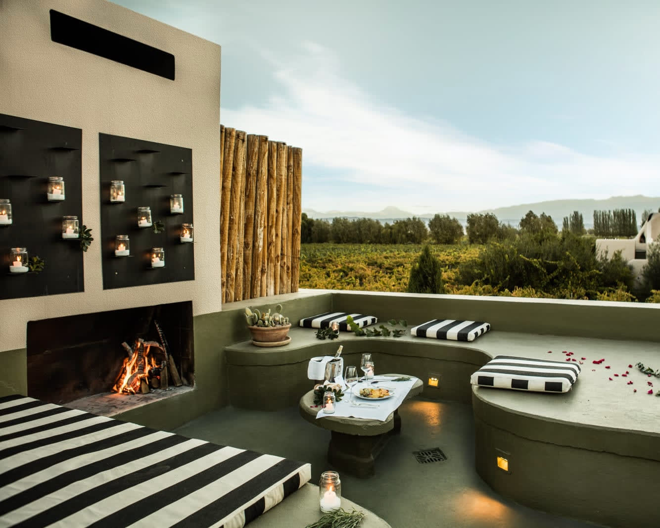 a rooftop lounge with padded seats, fireplace, candle lit wall, and cloudy daytime skies