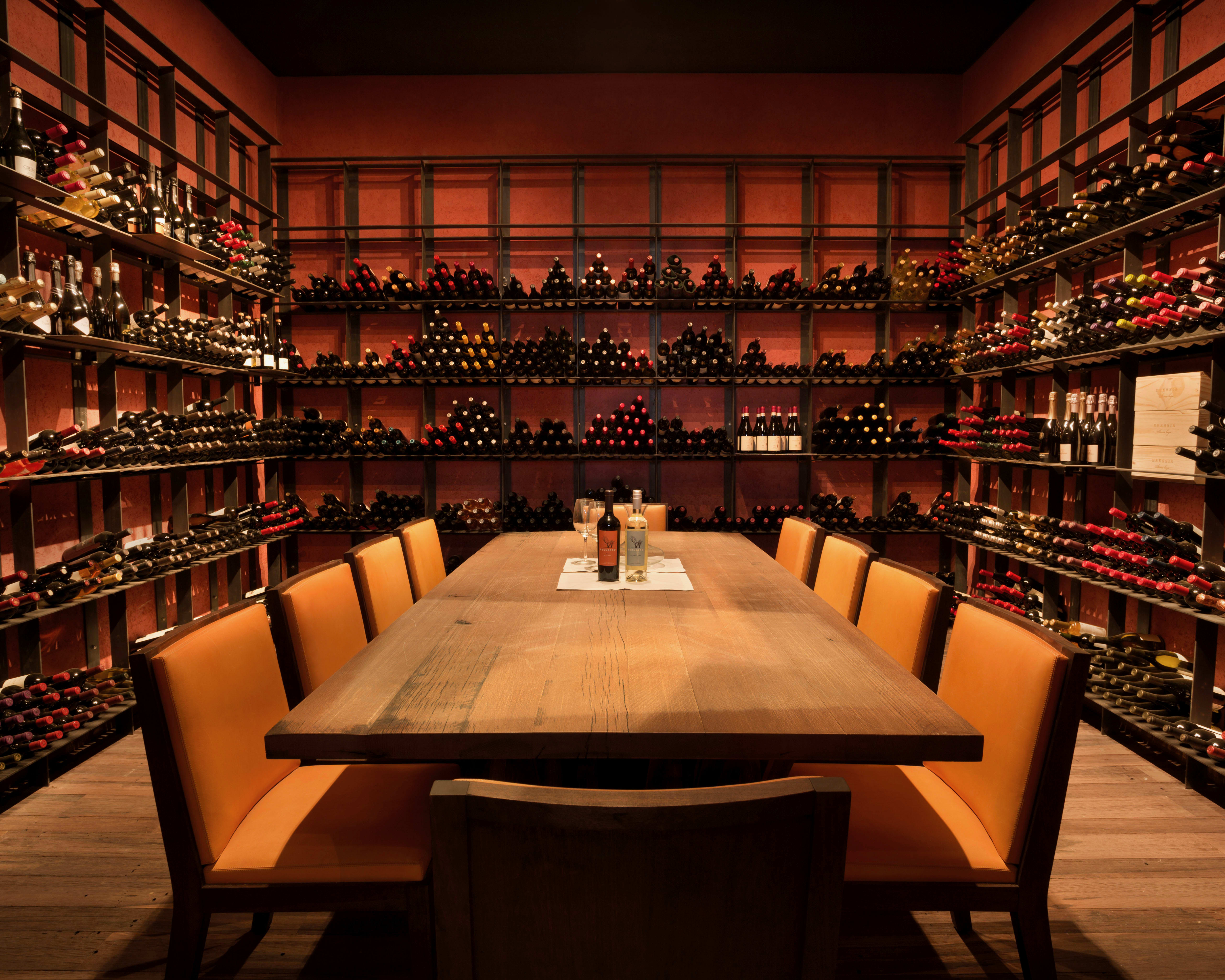 wood table and yellow chairs in a red walled room lined with shelves of wine bottles