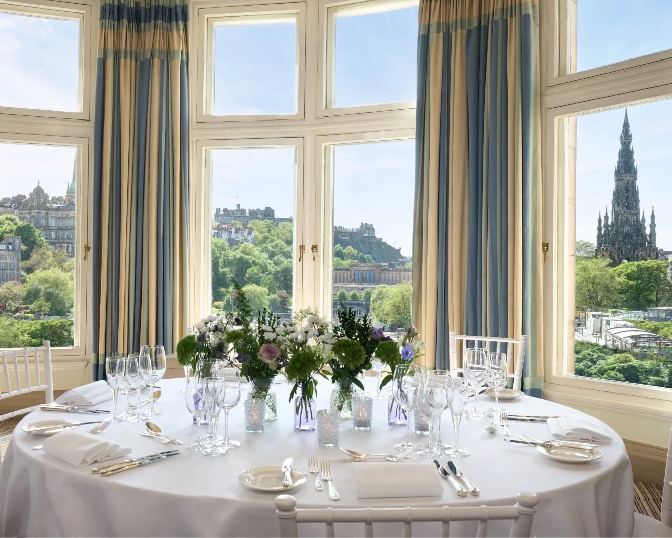 banquet table with dinner settings and chairs next to a window with a cityscape outside during day