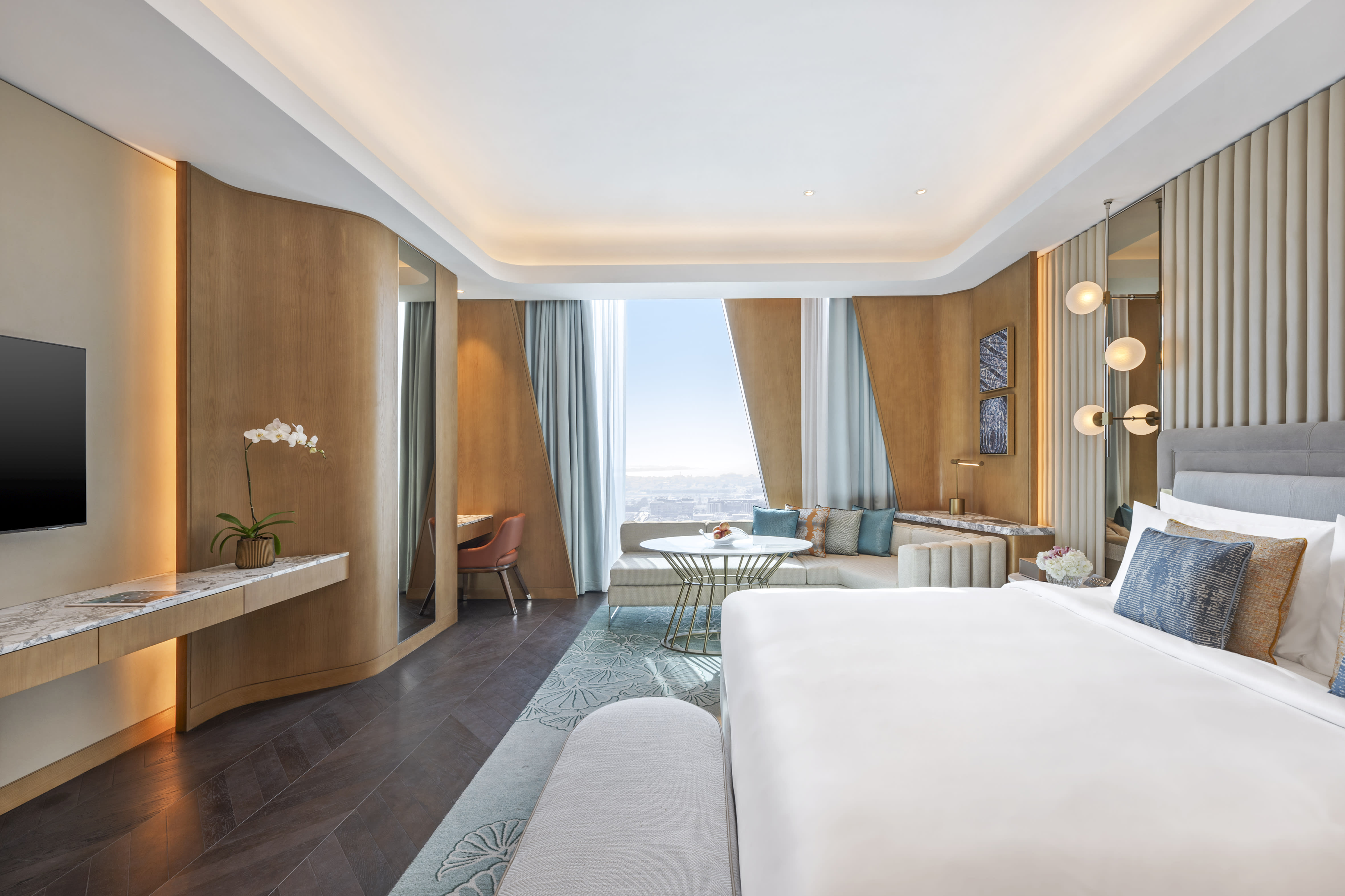 Contemporary hotel suite with sleek wood paneling, modern lighting, and a panoramic city view through floor-to-ceiling windows.