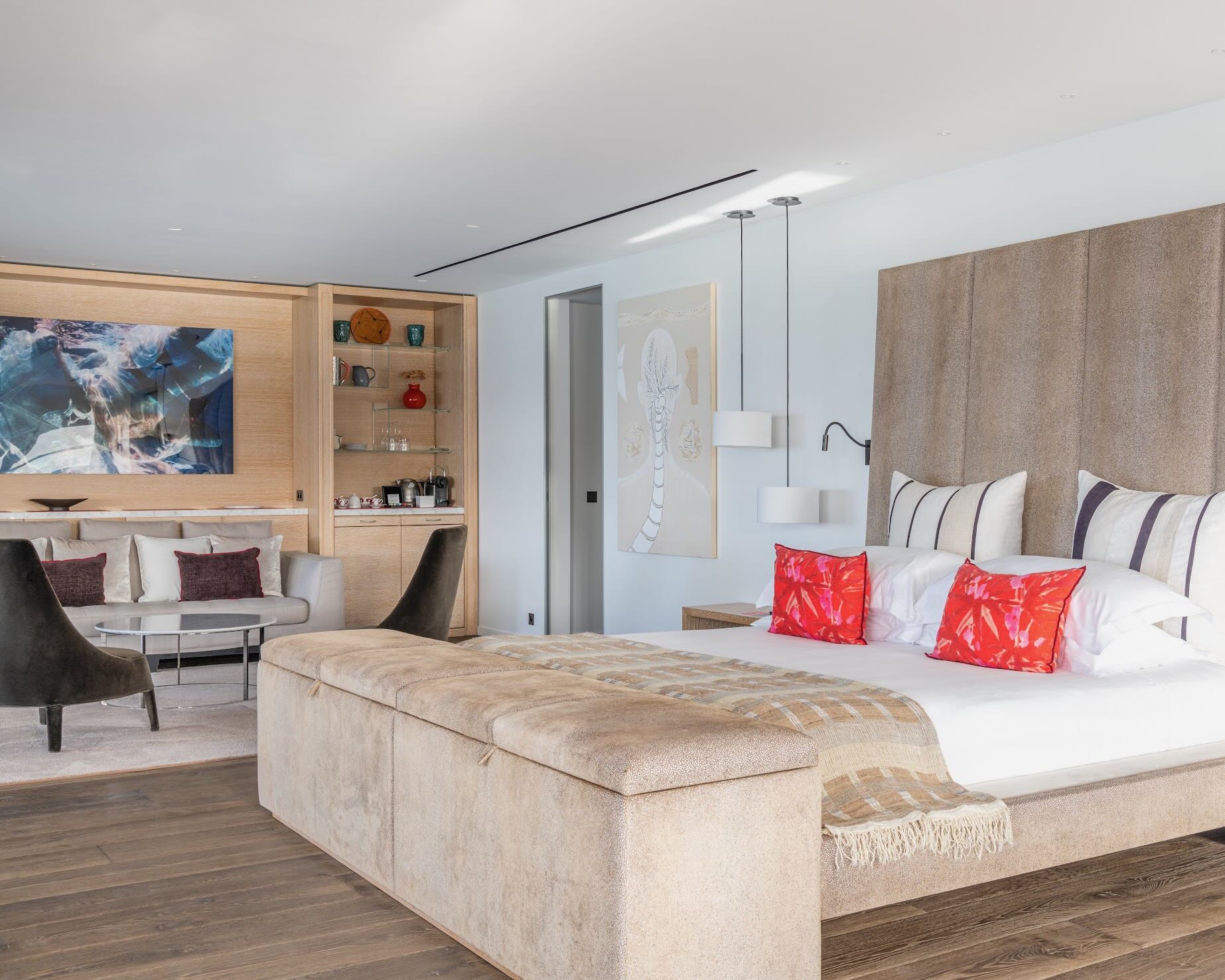 a modern neutral-colored hotel room with bed, wood floor, and seating area beneath artwork