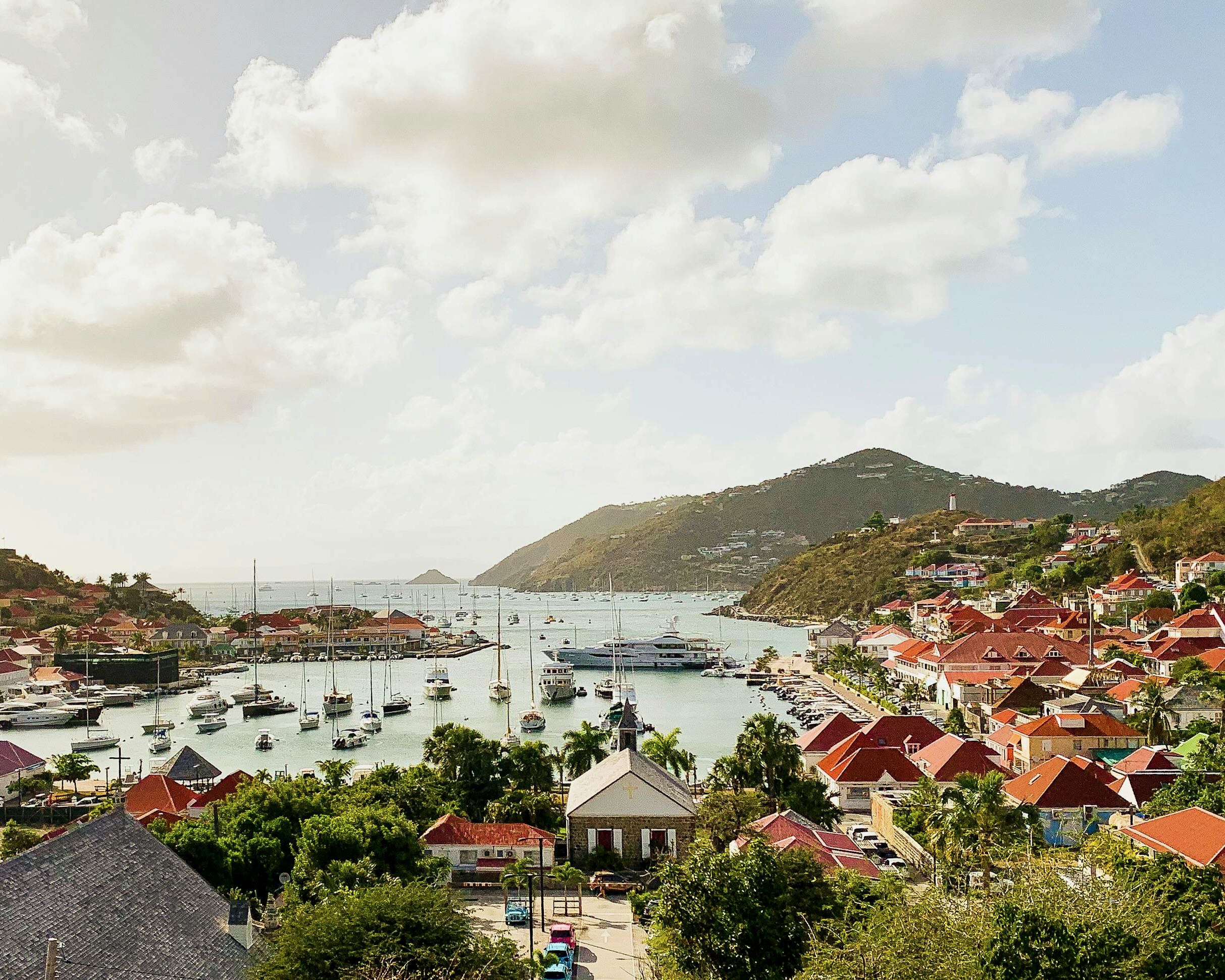 red roofed colonial buildings and palm trees overlooking a small harbor on a tropical island during day