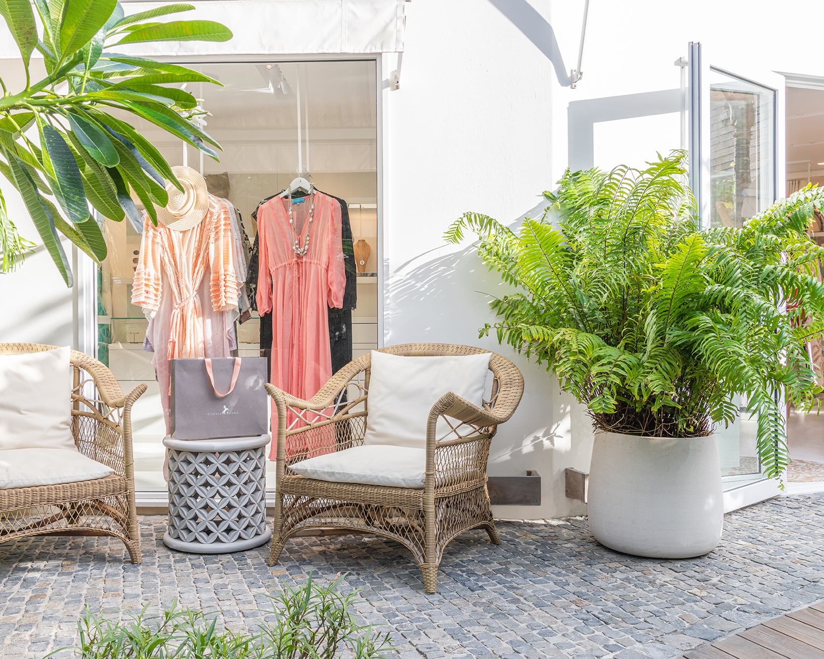 a clothing boutique with dresses hanging in the window, potted plants outside, and chairs outside