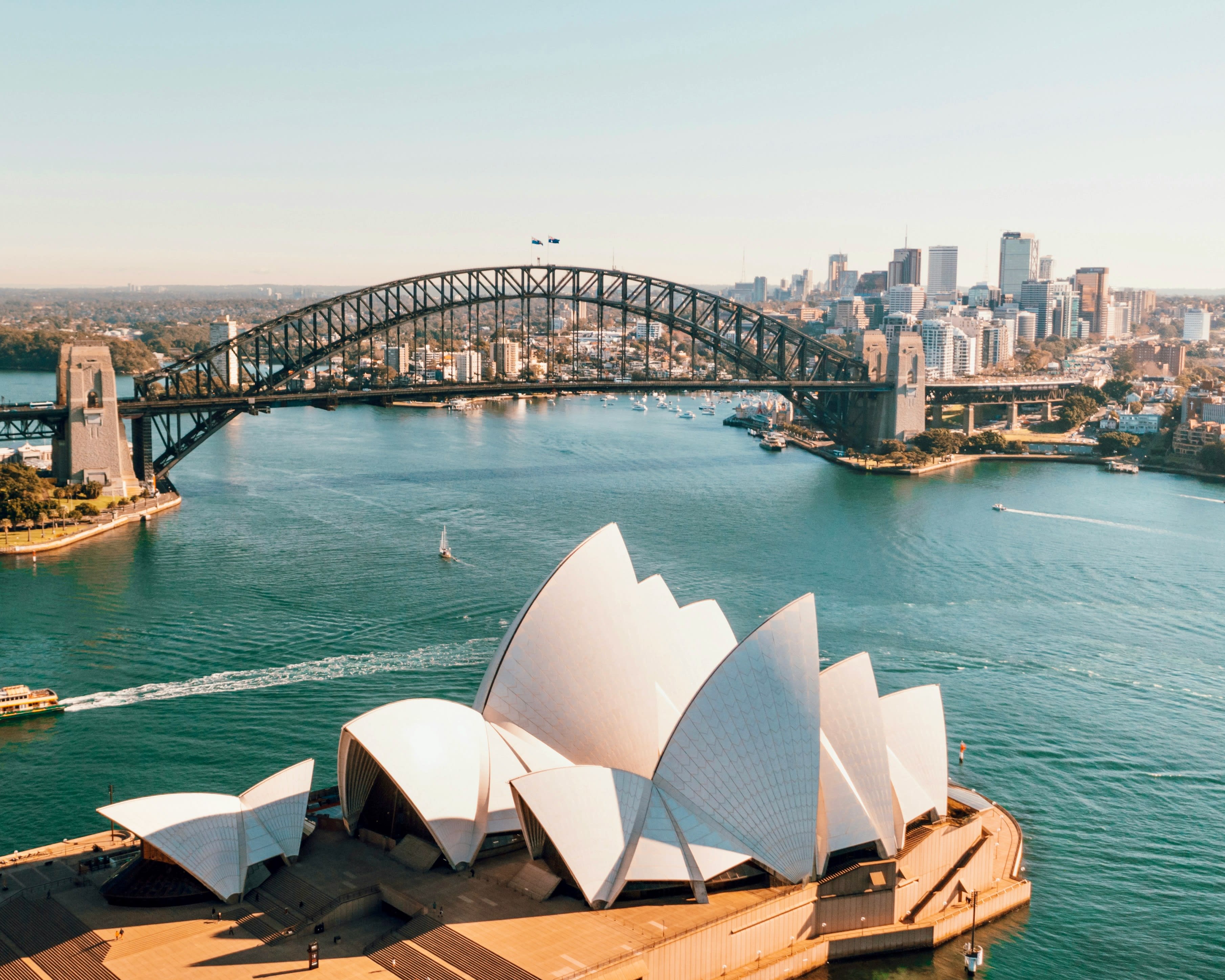 view of white sloped roofs next to a harbor with bridge and skyscrapers in the background